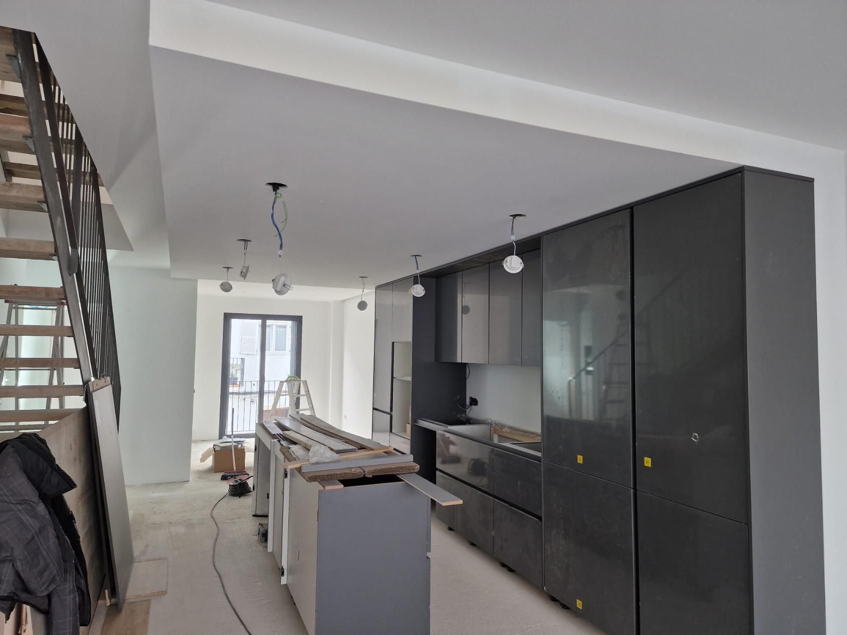 Una cocina moderna en construcción con gabinetes gris oscuro, una isla central y luces de techo a la vista