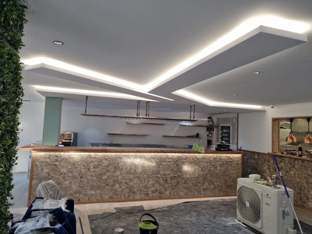 Una zona de bar con mostrador texturizado, iluminación bajo el mostrador y un diseño de techo con luces LED empotradas.