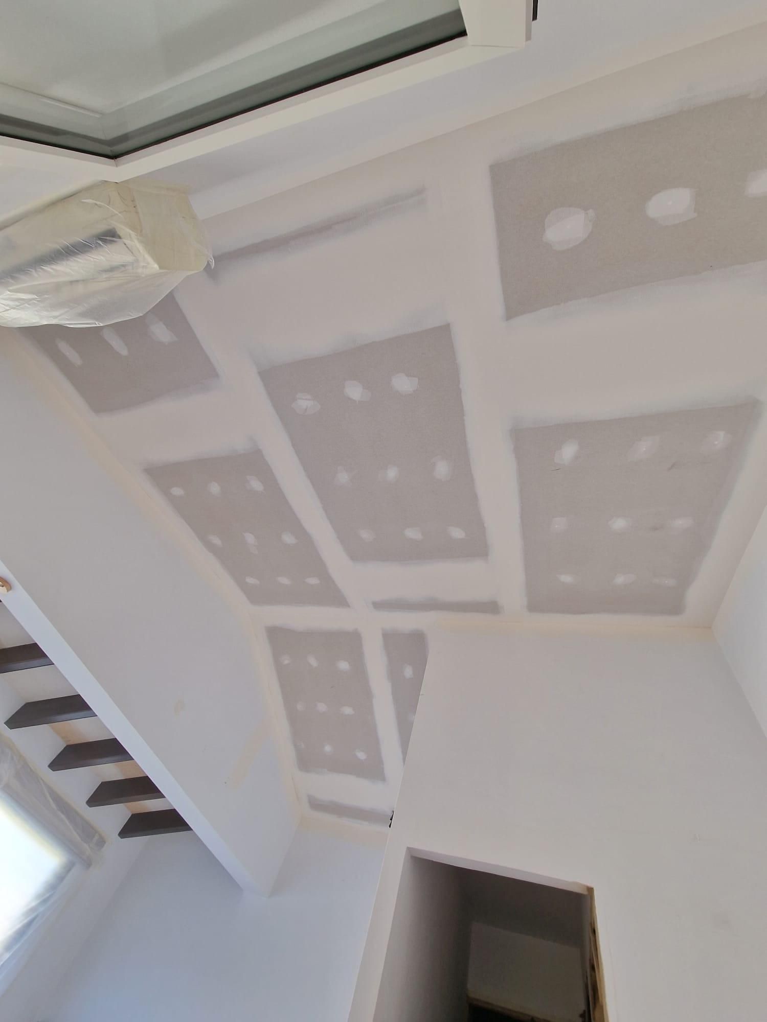 Vista desde un ángulo bajo de un techo blanco en construcción con varios parches rectangulares de paneles de yeso