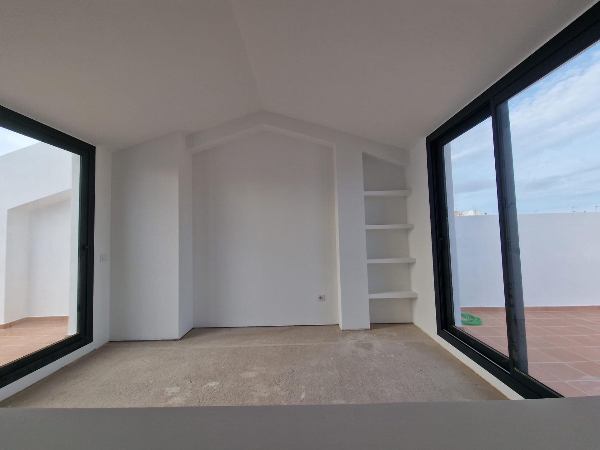 Una habitación minimalista con paredes blancas, suelo de baldosas beige, estanterías empotradas