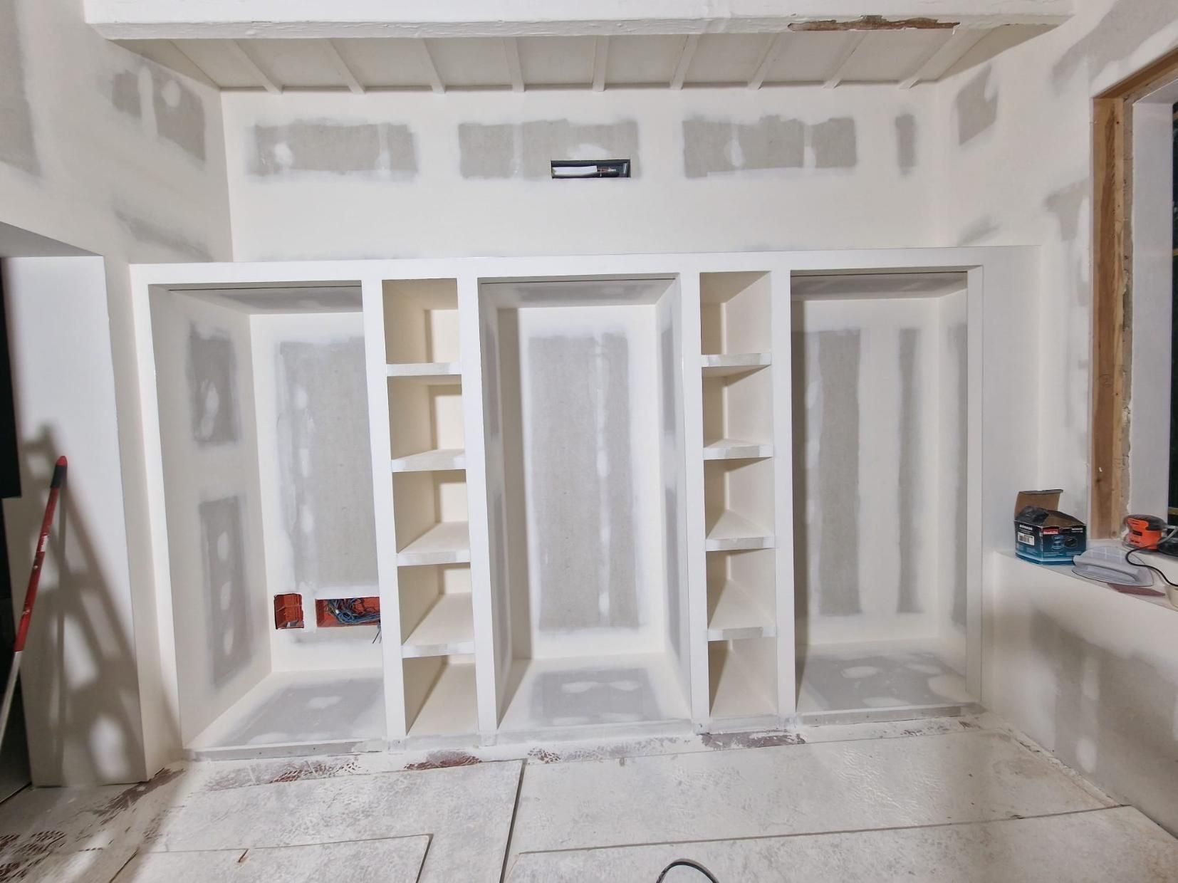 Una habitación en construcción que cuenta con un sistema de armarios de pladur recién instalado y pintado de blanco