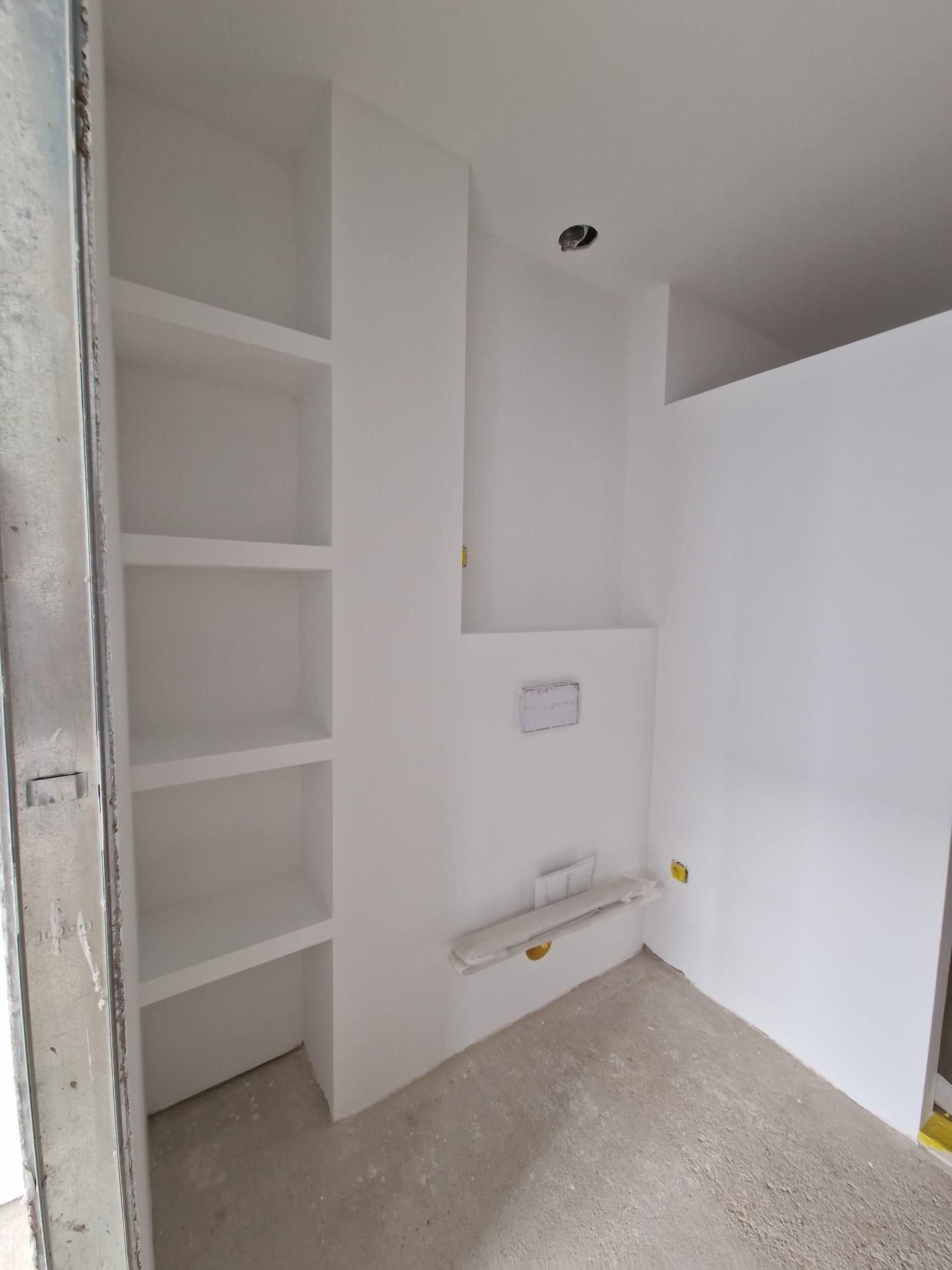 Una habitación en construcción con estantes blancos empotrados y accesorios eléctricos