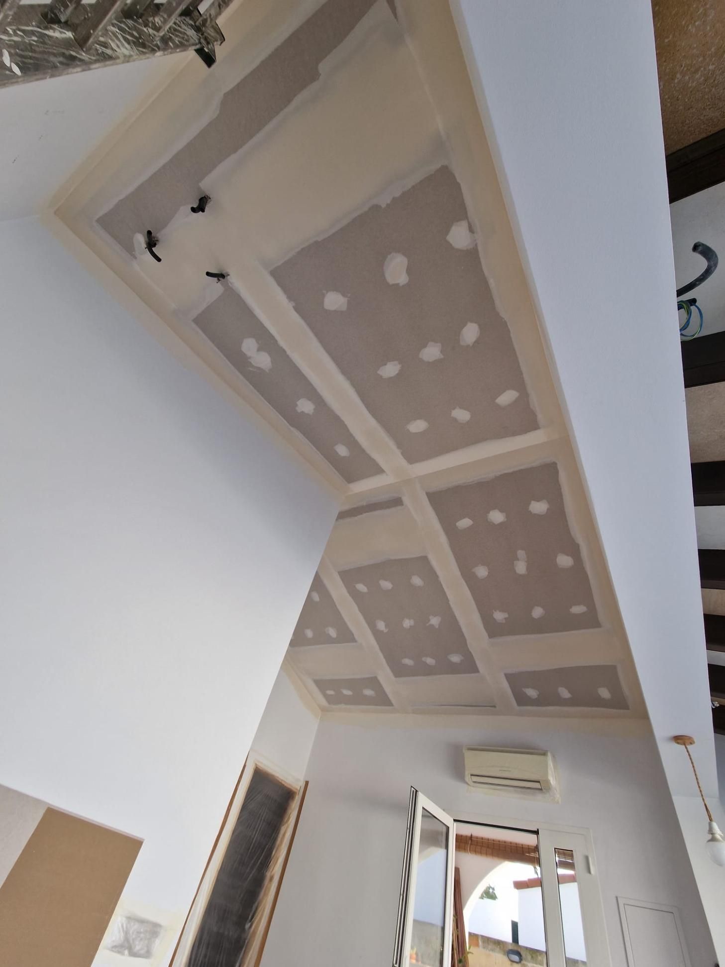 Un techo en construcción presenta secciones de paneles de yeso empotradas con tornillos y juntas de masilla visibles.