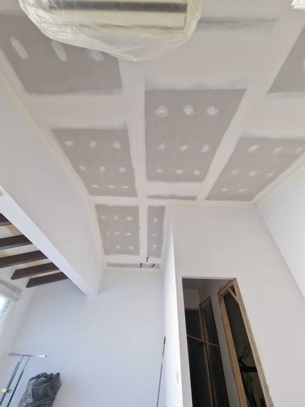 Una habitación en construcción con paneles de pladur blanco en el techo, donde se aprecian las juntas