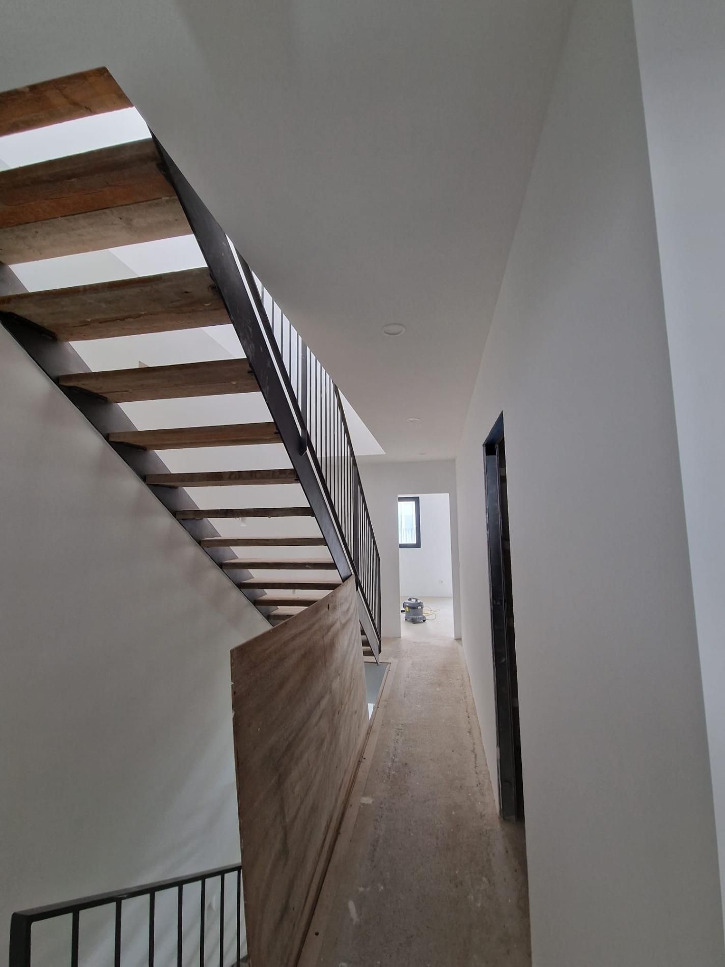 Un pasillo con escaleras de madera a la izquierda, una barandilla de metal