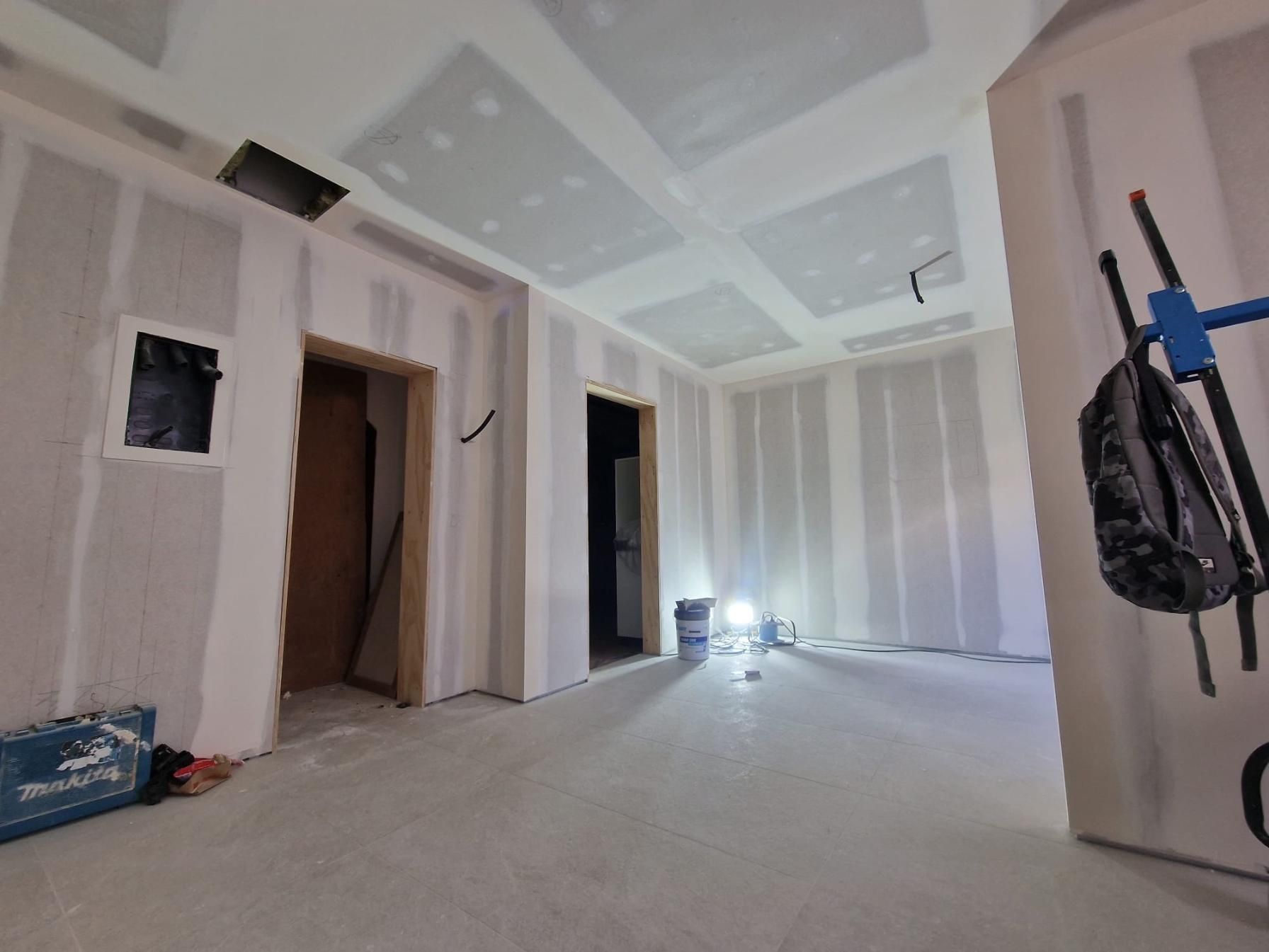 Una habitación sin terminar con paredes y techo de pladur, que incluye dos puertas y una lámpara de trabajo en el suelo.