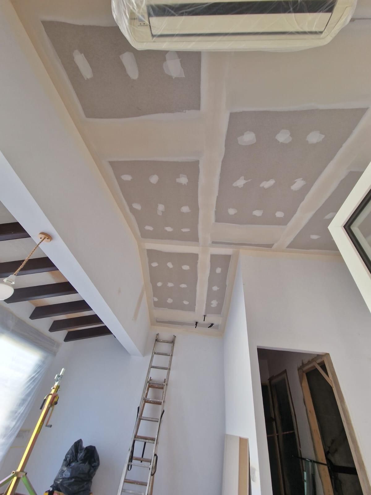 Vista interior de una habitación en proceso de renovación, con un techo de pladur parcialmente terminado con juntas selladas