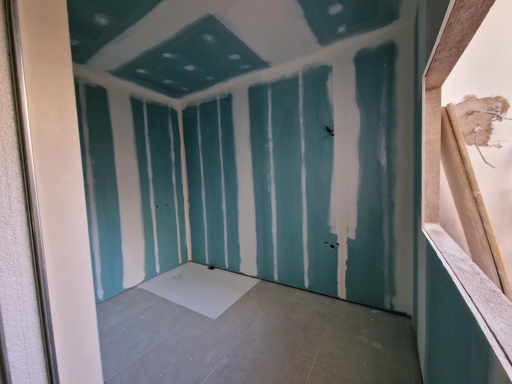 Una habitación en construcción con paneles de yeso verdes resistentes a la humedad y juntas selladas con cinta blanca.