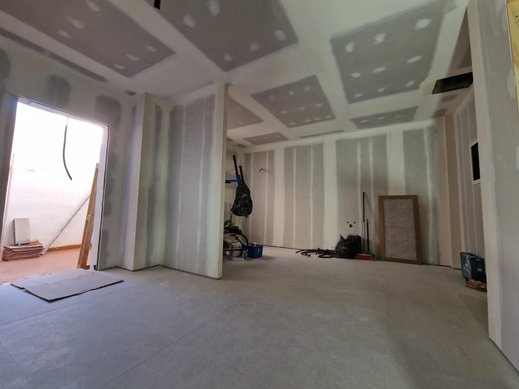 Una habitación en construcción con paneles de yeso sin terminar en paredes y techos, que deja ver la estructura de montantes