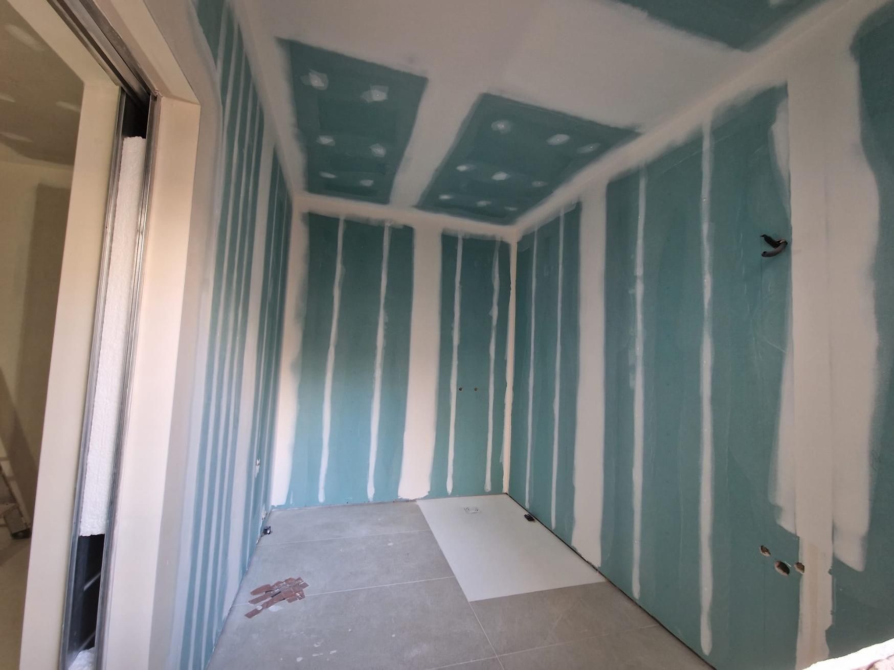 Vista interior de una habitación en construcción con paneles de yeso resistentes a la humedad de color turquesa .