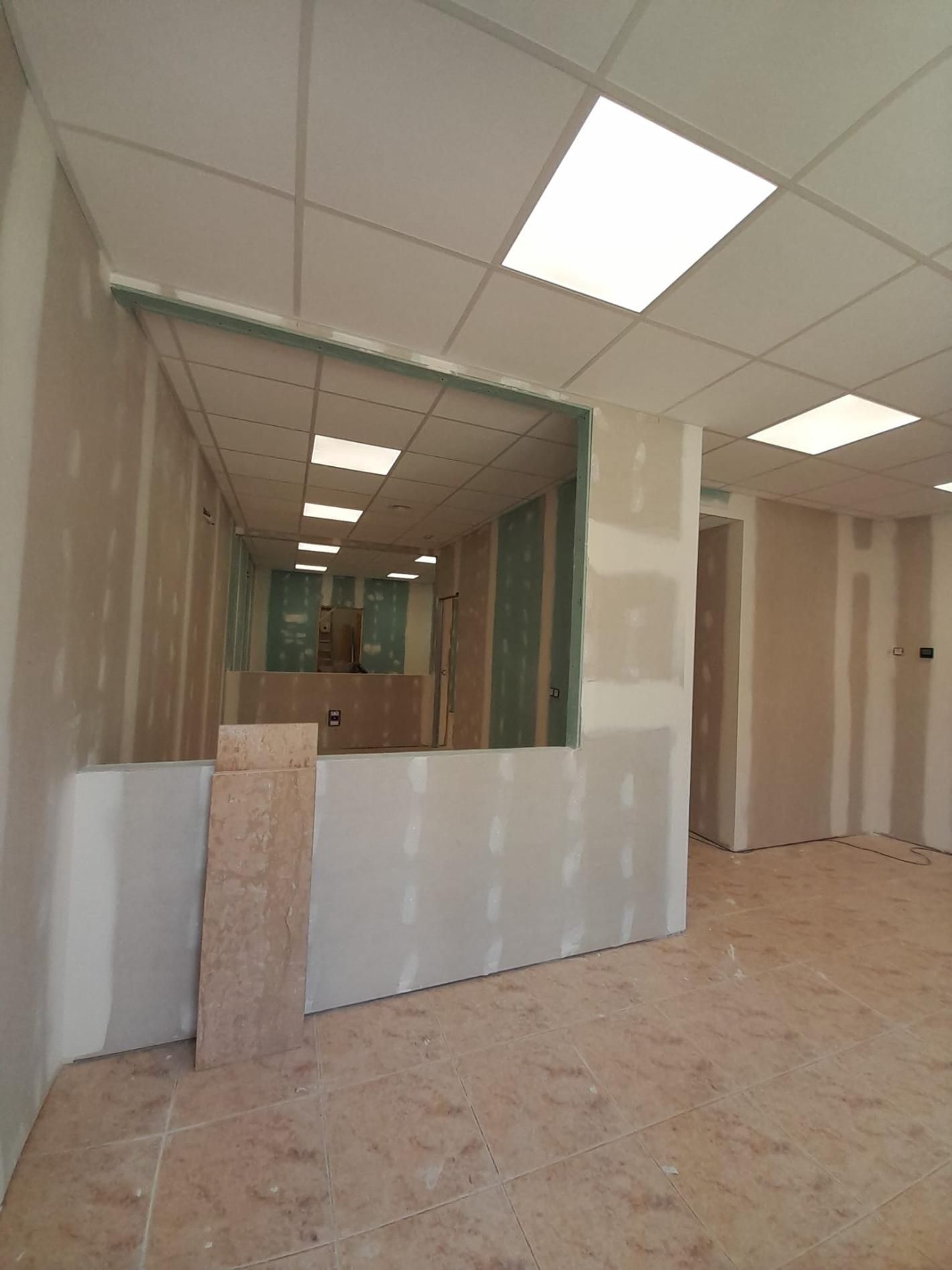 Una obra en construcción con paredes de pladur sin terminar, estructura metálica y paneles de techo suspendido instalados.