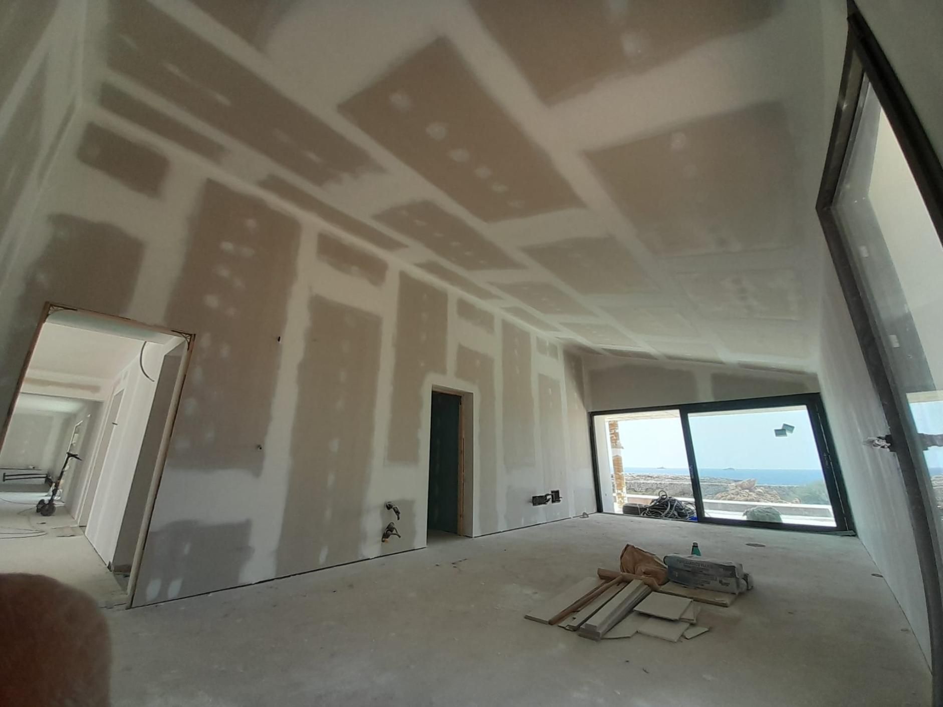 Una habitación interior en construcción con paneles de yeso recién instalados y juntas selladas en las paredes y el techo.