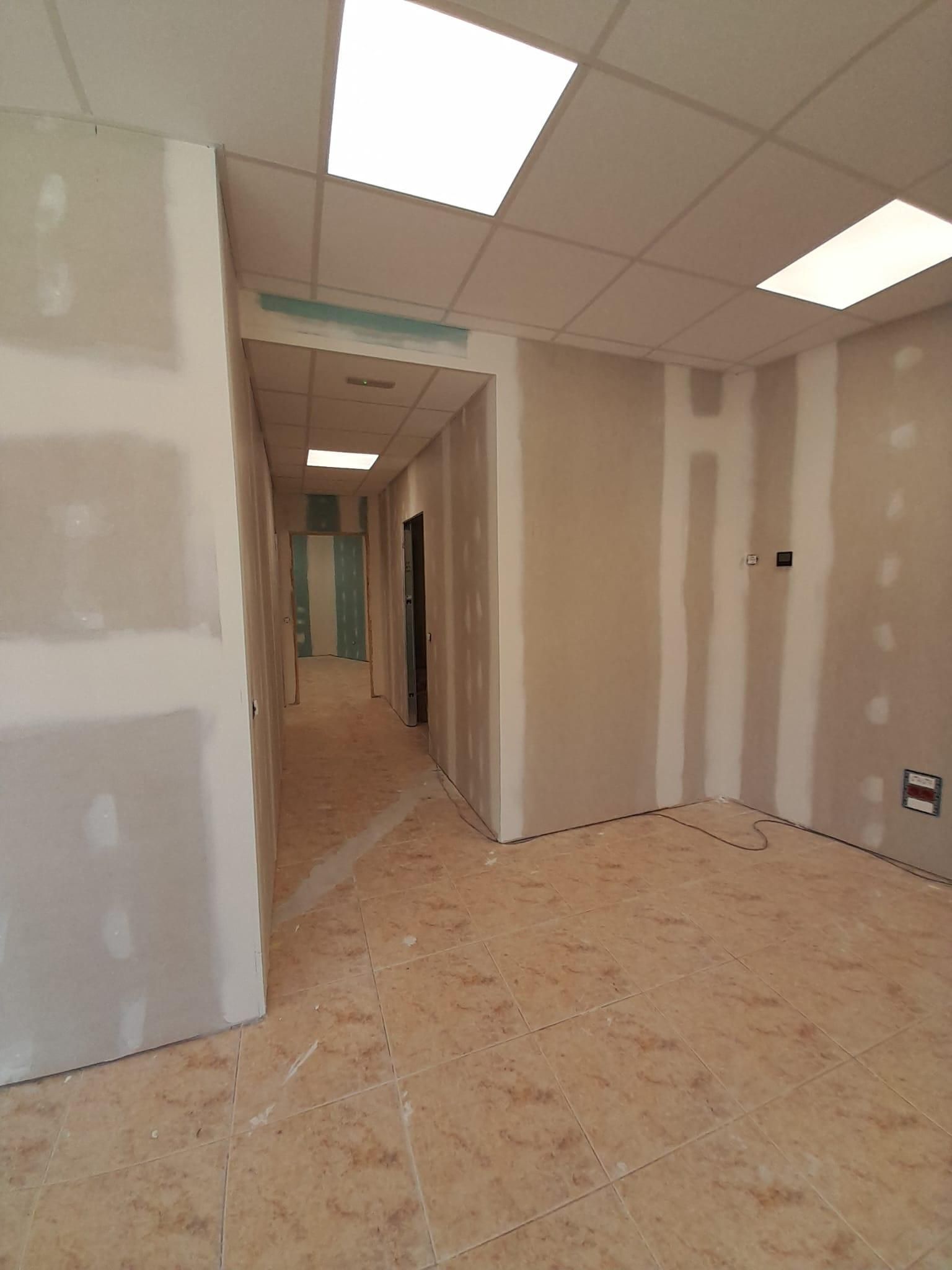 Vista interior de un pasillo en construcción con paneles de yeso sin terminar, juntas expuestas y un falso techo.