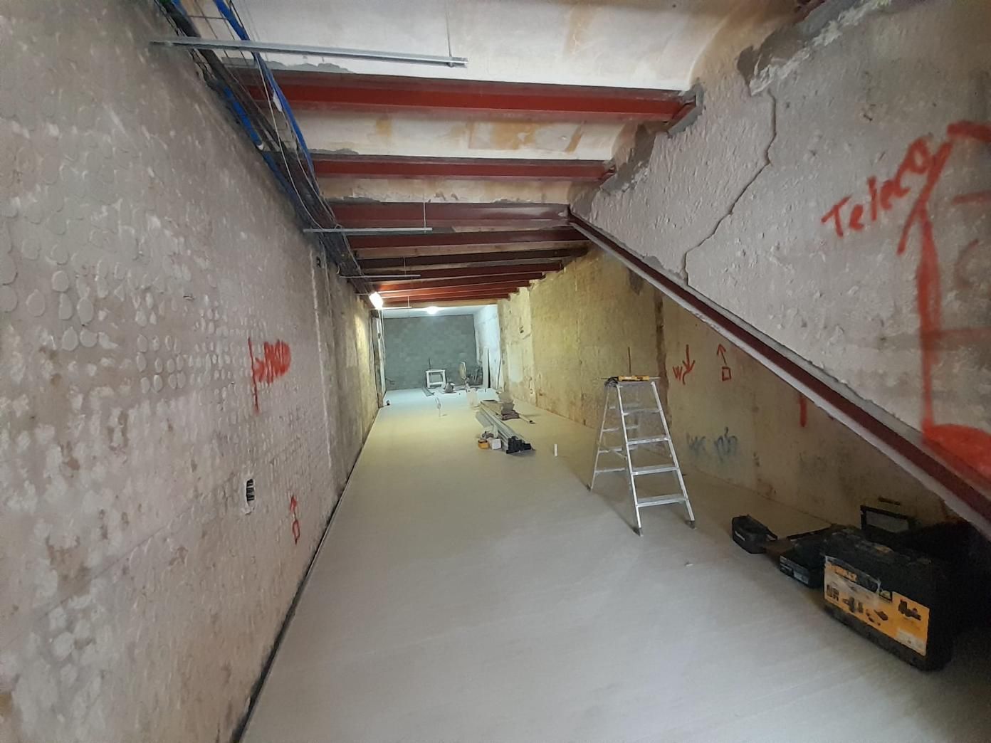 Un estrecho pasillo de construcción con vigas pintadas de rojo en el techo, paredes sin terminar