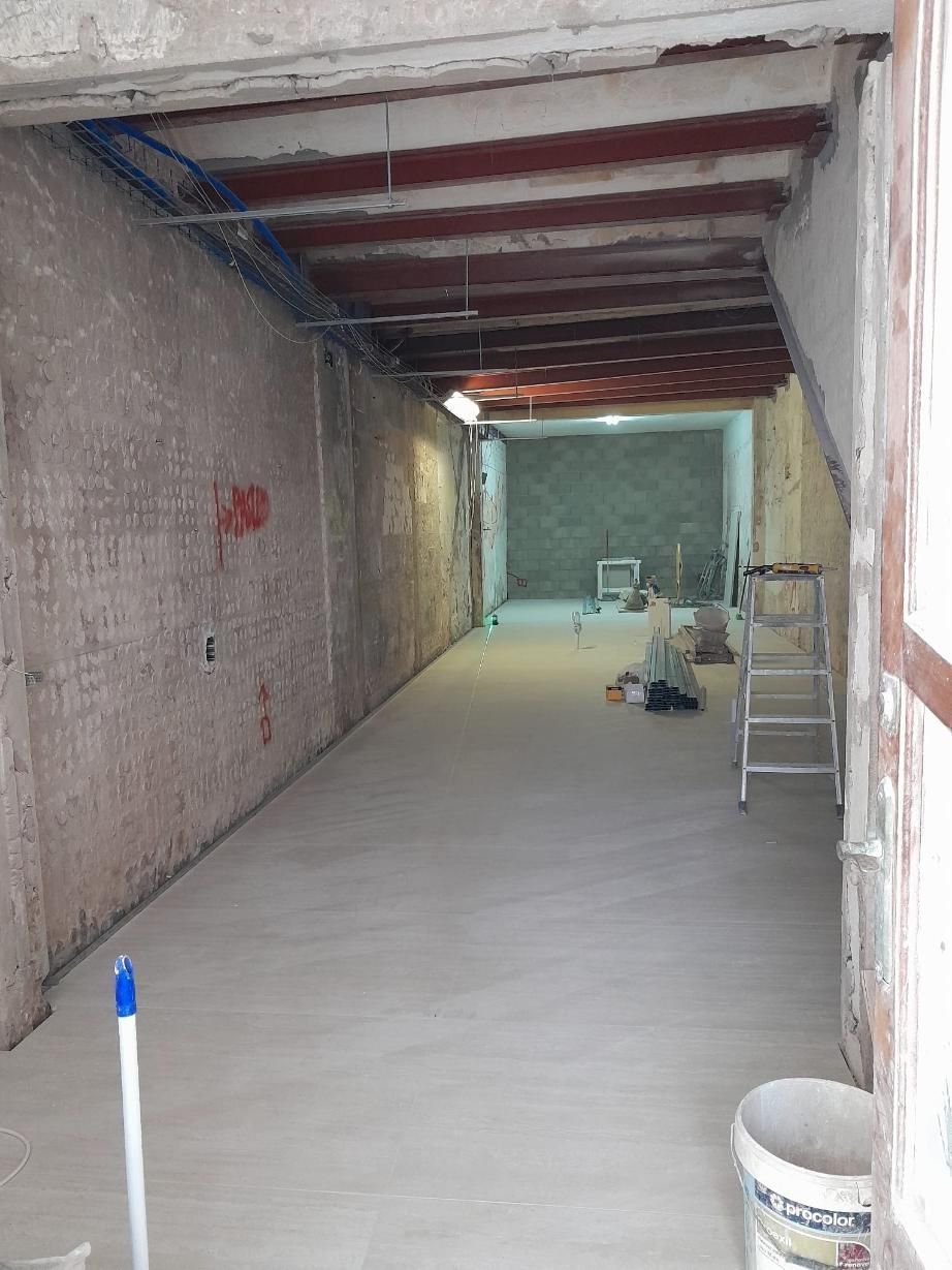 Una habitación larga y estrecha en proceso de renovación, con paredes de ladrillo visto, techo parcialmente terminado