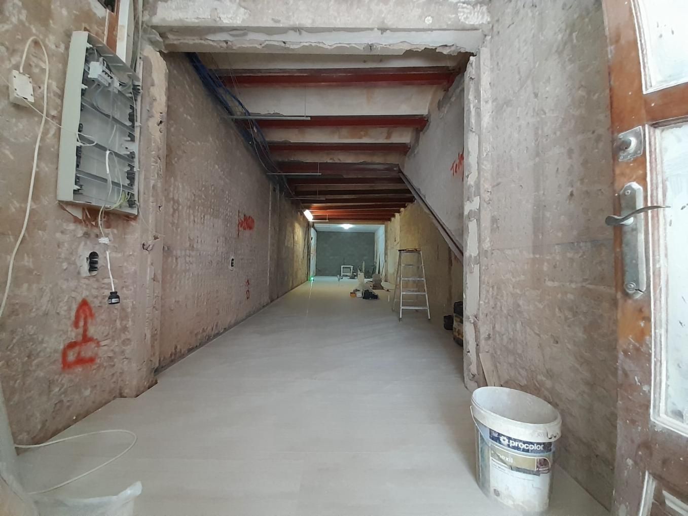 Un pasillo estrecho en obras, con paredes de ladrillo visto, vigas de madera expuestas en el techo, suelo claro