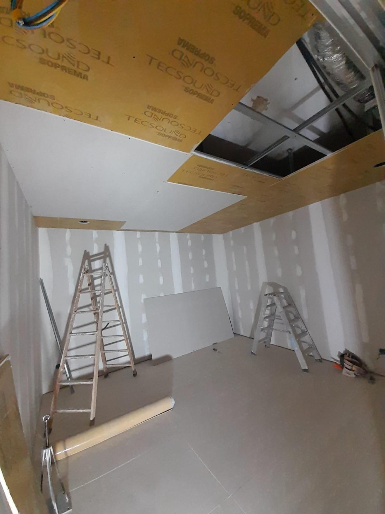 Habitación interior en proceso de renovación con paredes de pladur blanco, un techo acústico parcialmente instalado