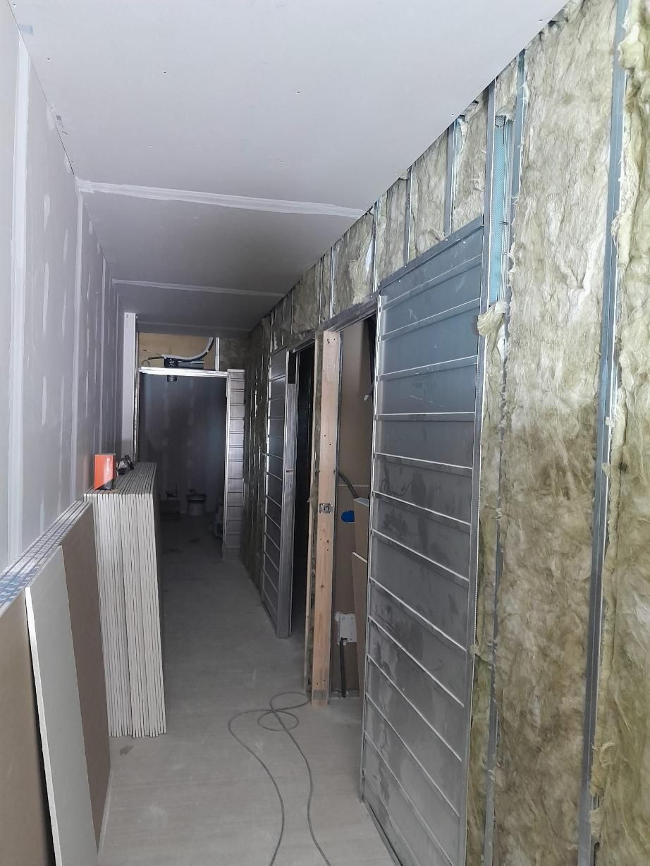 Un estrecho pasillo interior de obra con paredes de pladur al descubierto en un lado y montantes metálicos