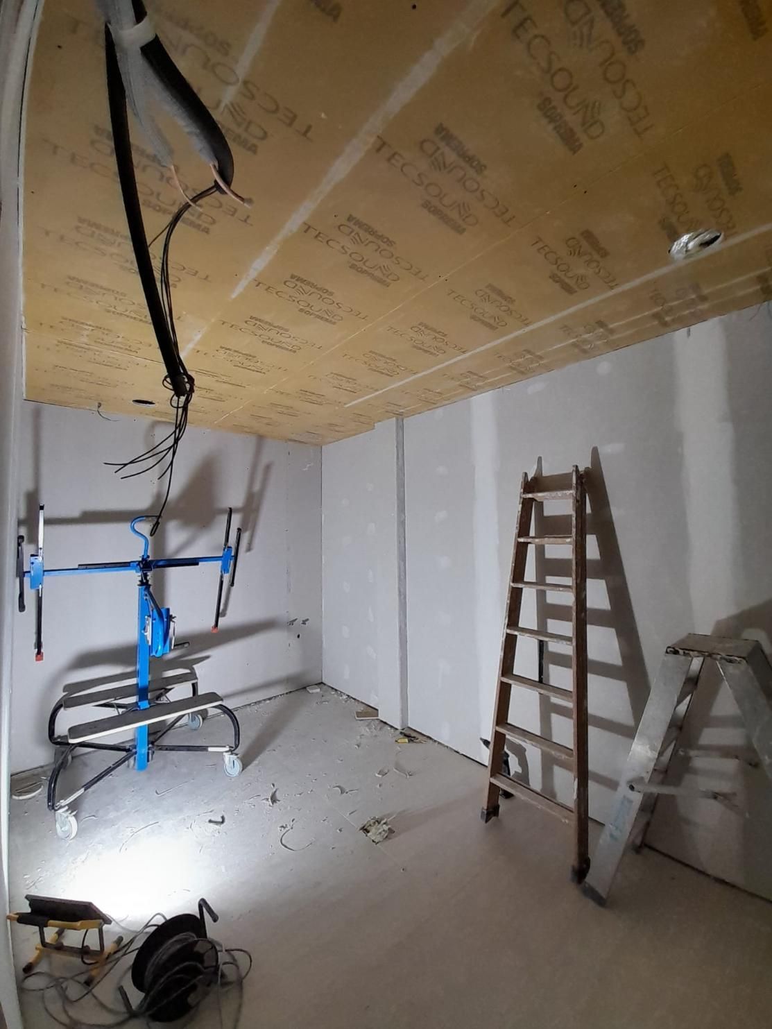 Una habitación sin terminar con un panel en el techo, una plataforma elevadora de pladur azul