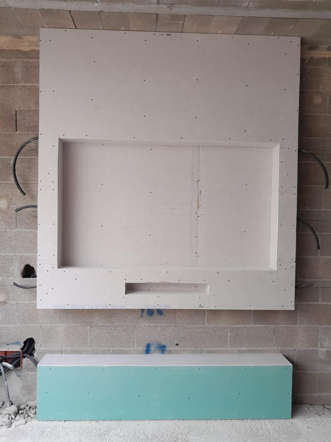 Una pared decorativa de pladur parcialmente construida, con un gran nicho para la televisión y un mueble de almacenamiento