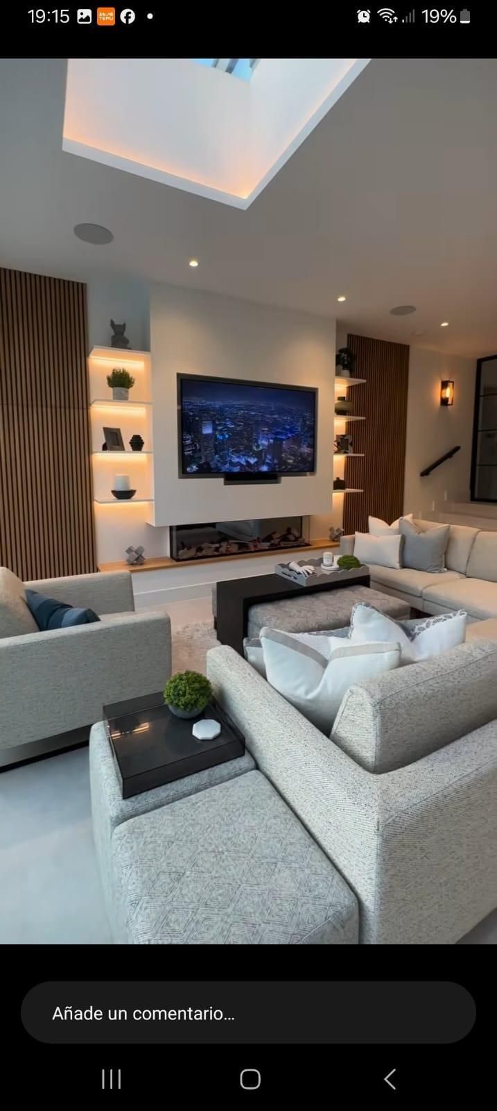 Un salón contemporáneo con televisor montado en la pared, estanterías iluminadas integradas