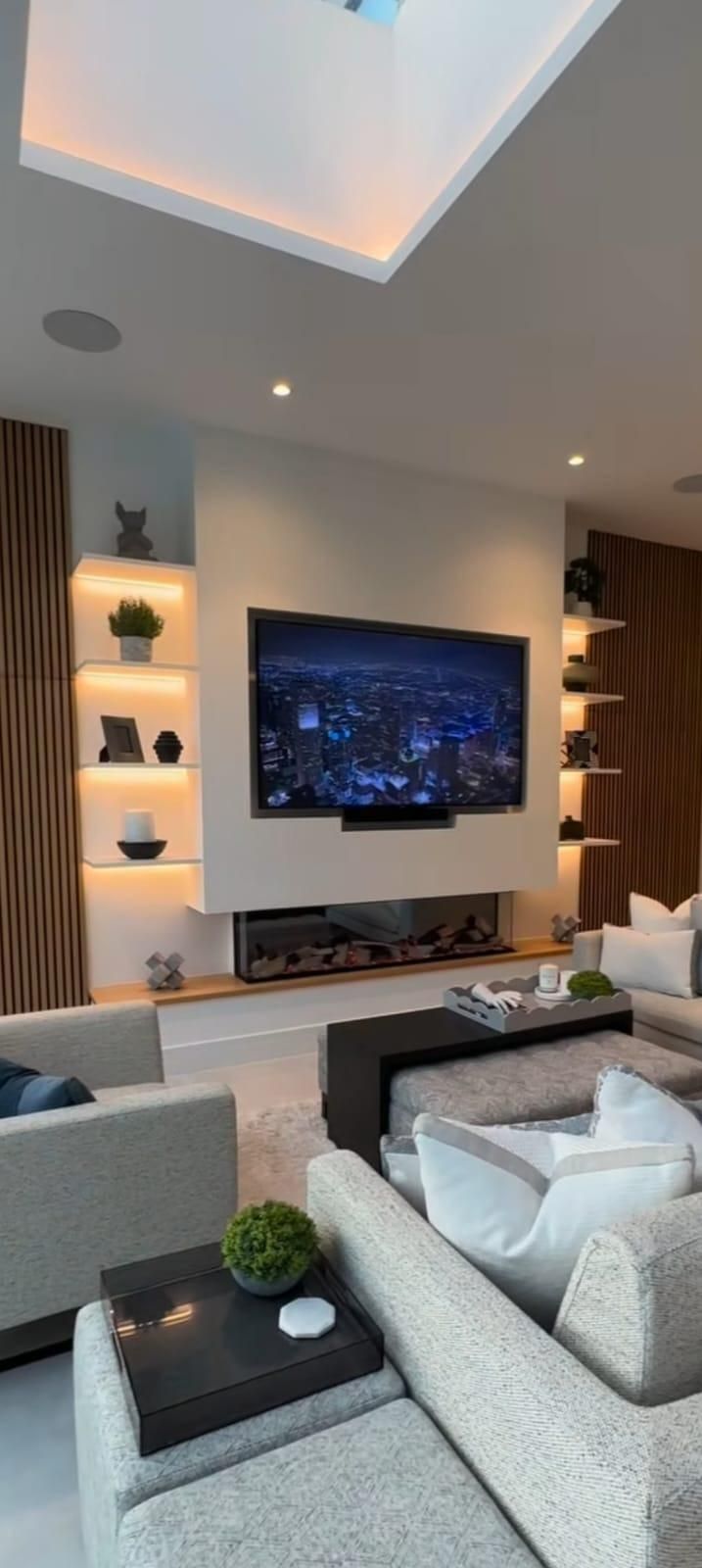 Un salón moderno con televisor montado en la pared, estanterías iluminadas, chimenea y muebles de asiento en tonos neutros.
