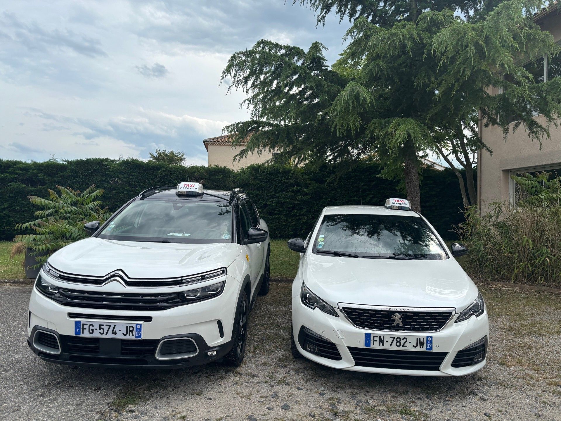 Deux taxis blancs garés côte à côte à l'extérieur. Une Citroën et une Peugeot, toutes deux équipées de gyrophares de taxi.