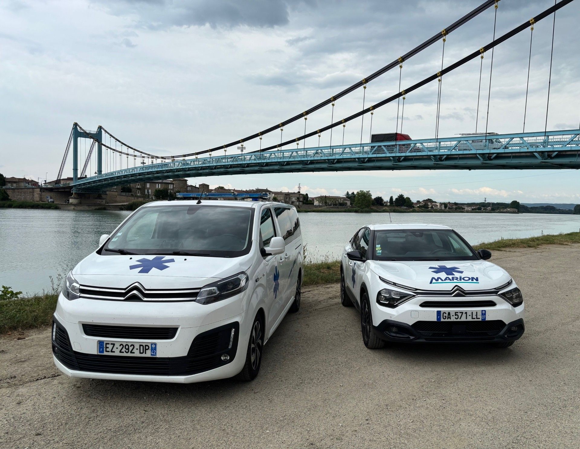 Deux véhicules médicalisés Citroën des Ambulances Marion arborant des emblèmes médicaux sont stationnés près d'un pont et d'un cours d'eau.