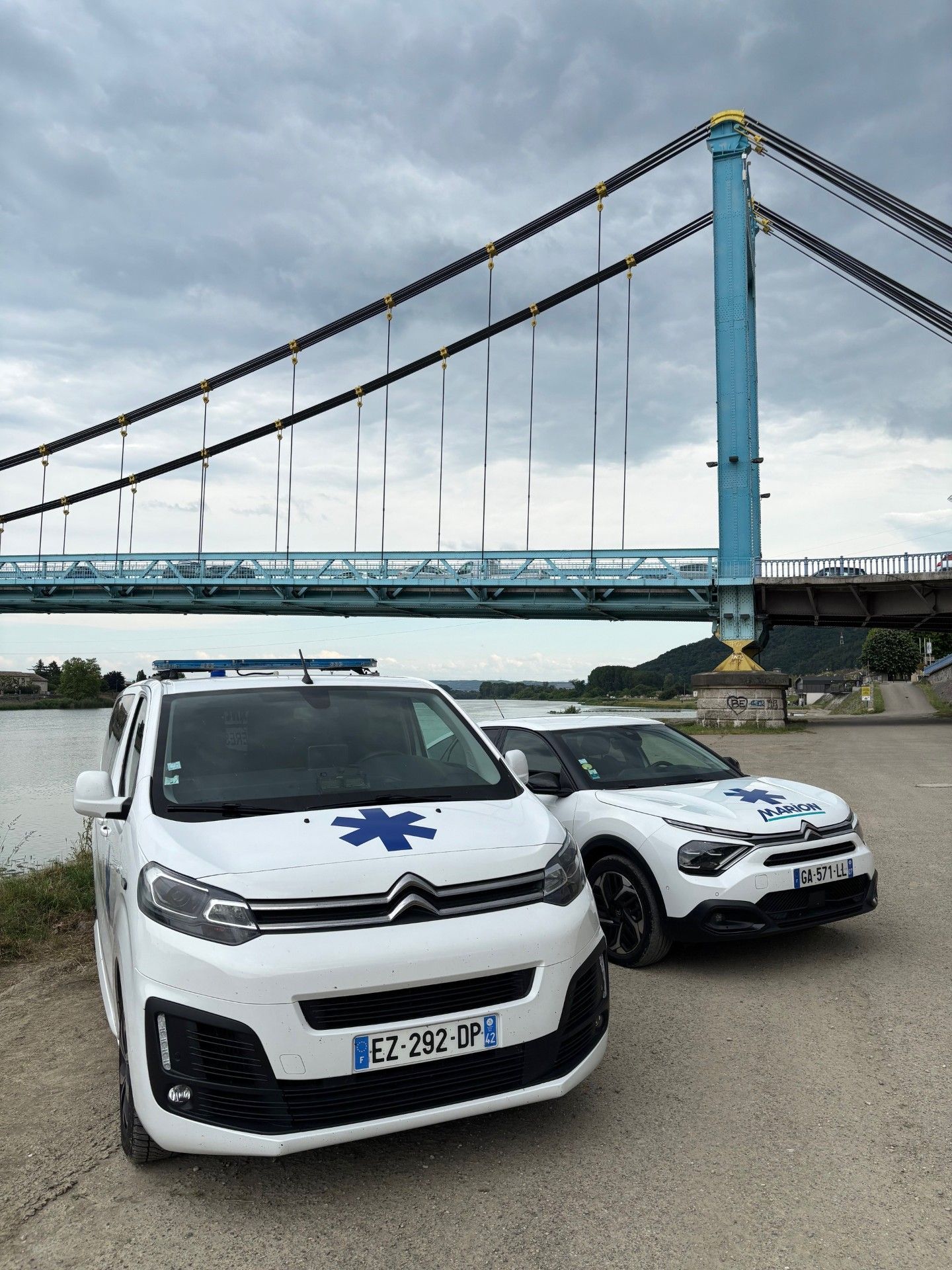 Deux véhicules d'urgence Citroën blancs stationnés devant un pont bleu, ciel couvert.