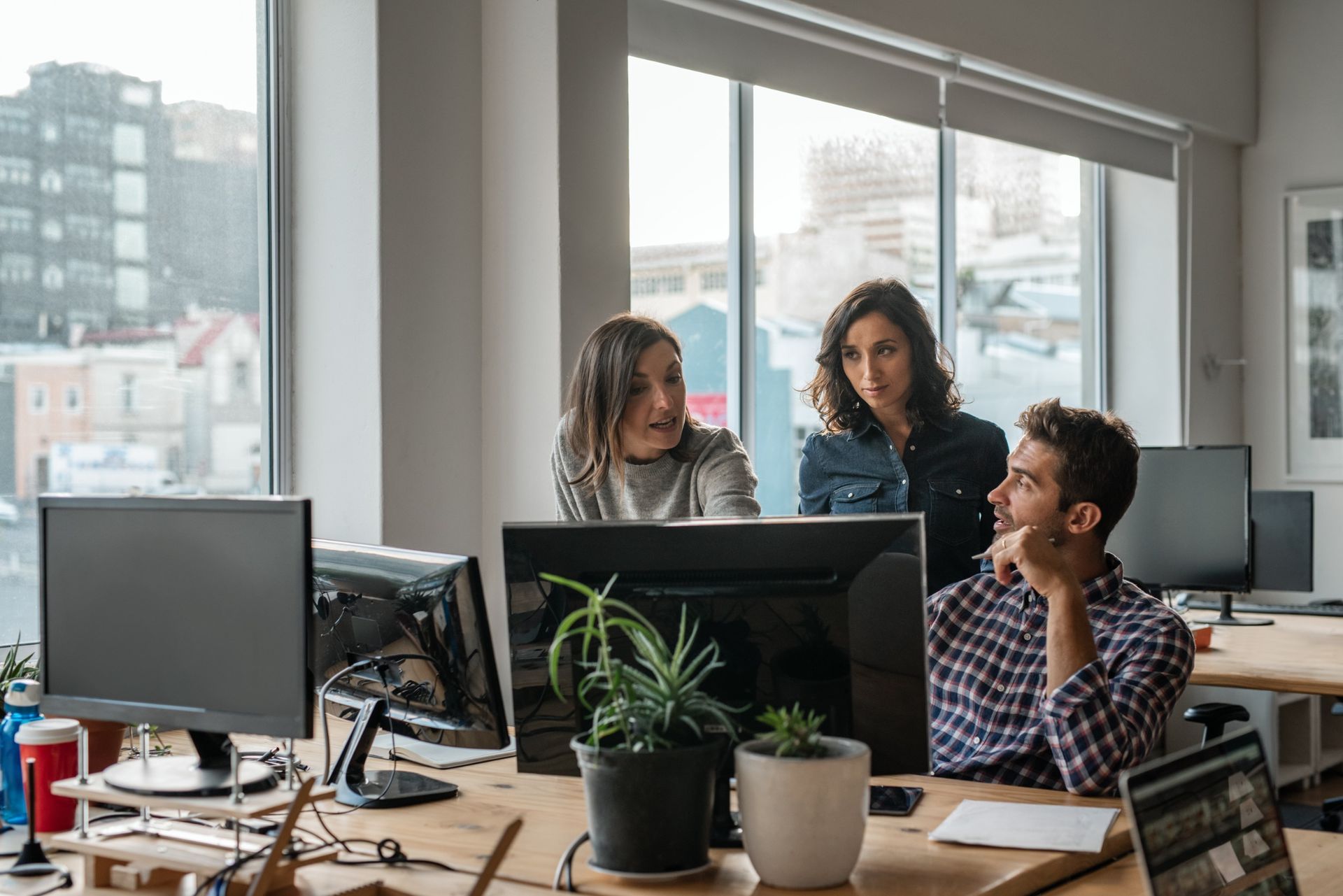 Un grupo de personas están sentadas en escritorios frente a monitores de computadora en una oficina.