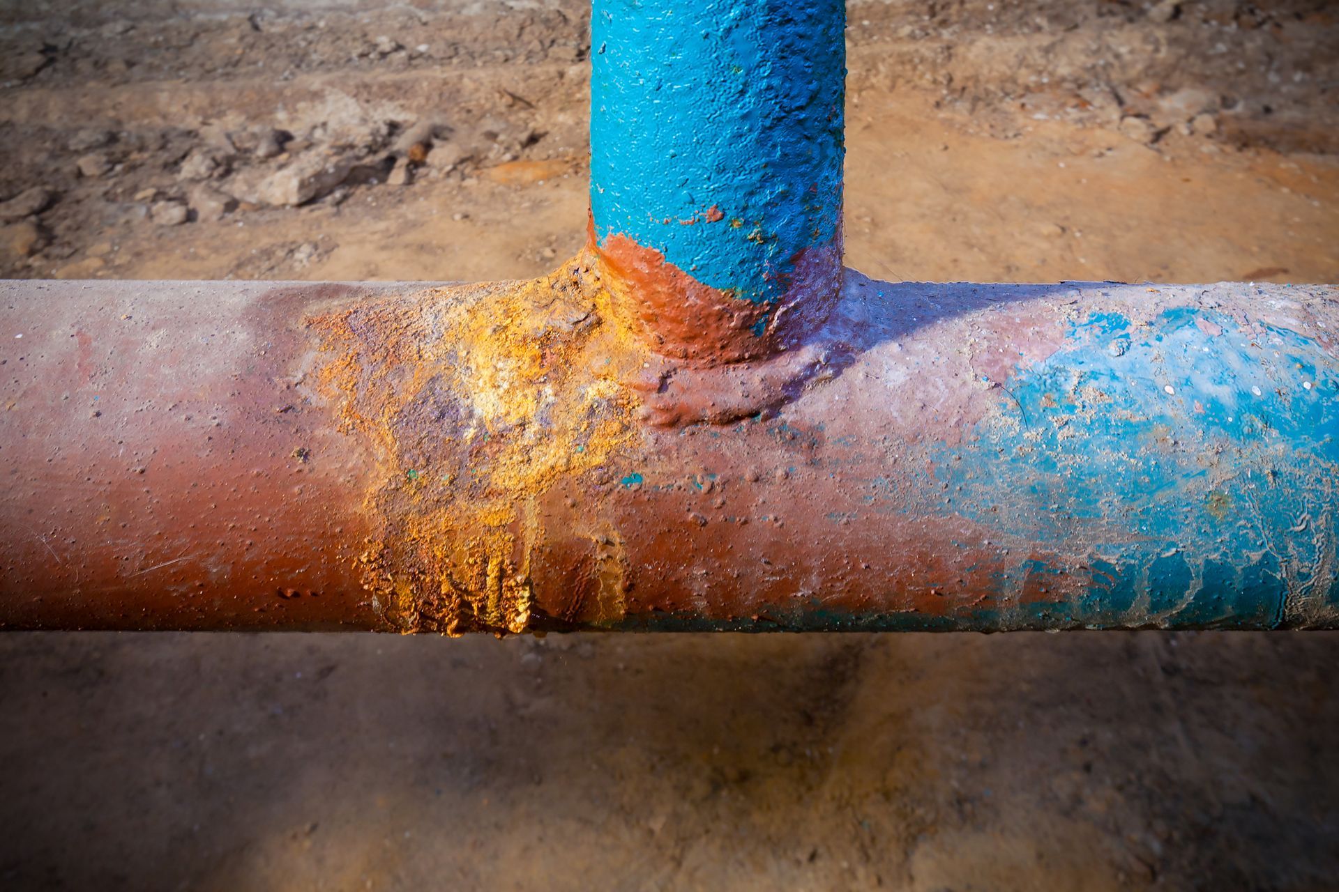 Tuyau métallique peint en bleu et orange, présentant de la corrosion, un raccord en T.