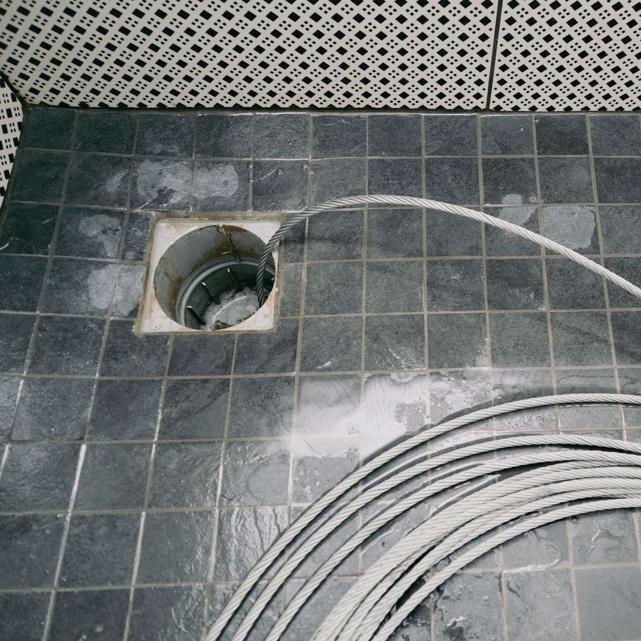 Câble enroulé sur un sol carrelé, s'étendant dans une canalisation.