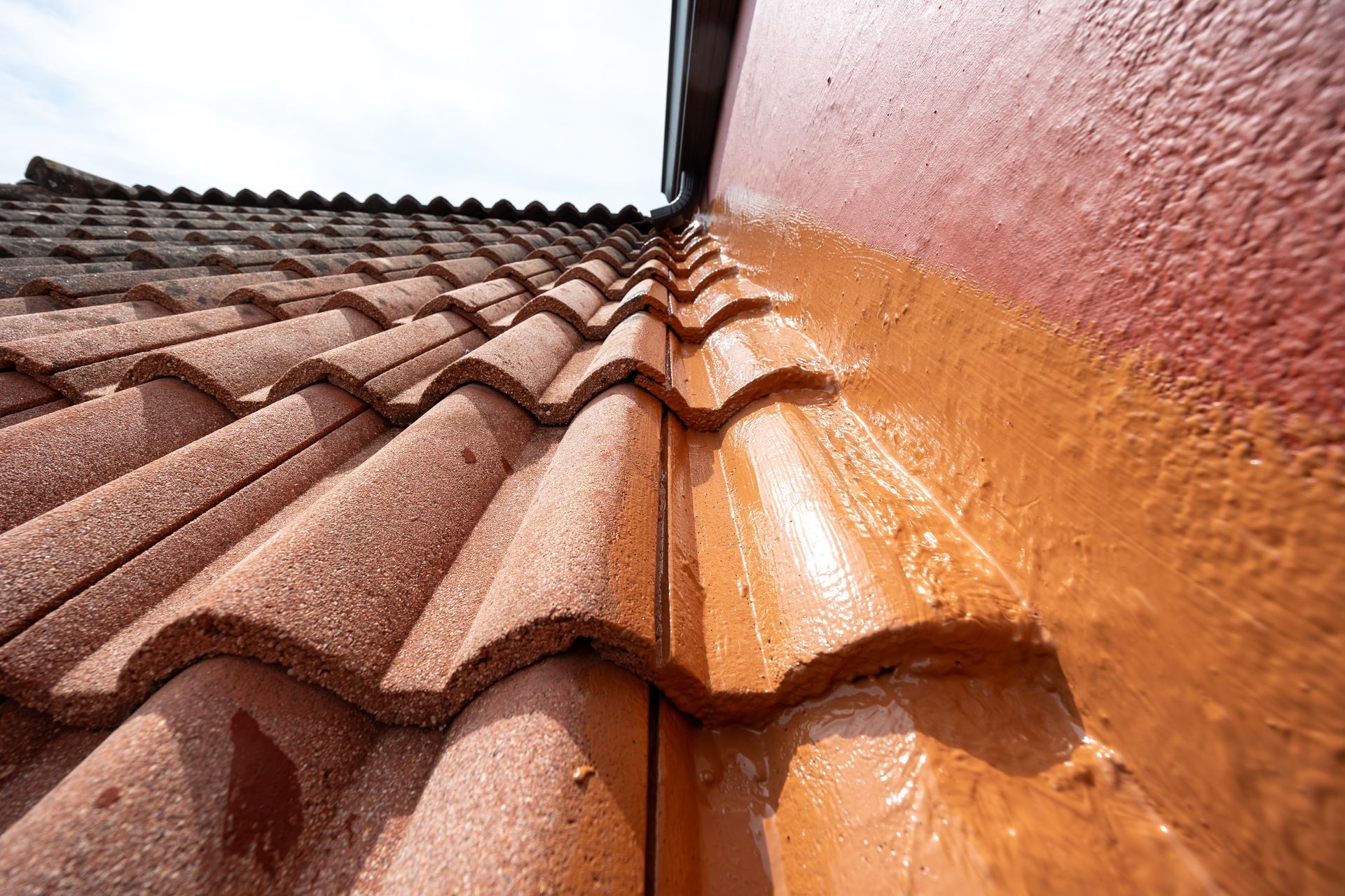 Un toit de tuiles rouges côtoie un mur rouge recouvert d'un mastic humide.