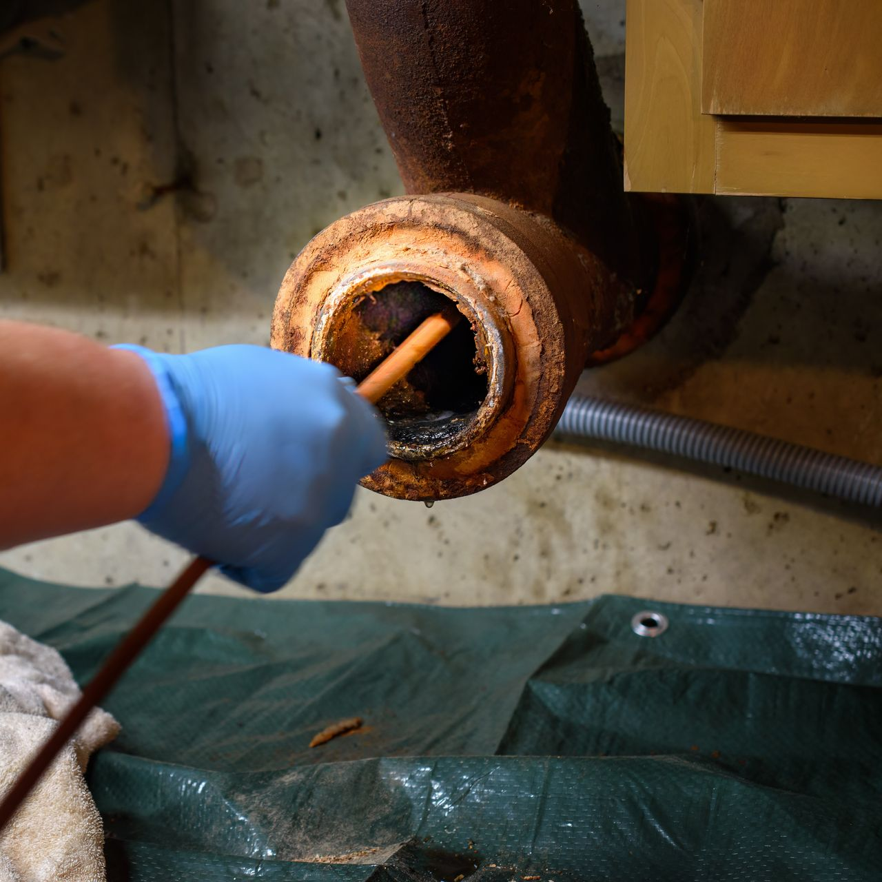 Main gantée sondant un tuyau corrodé à l'aide d'un outil, dans un sous-sol.
