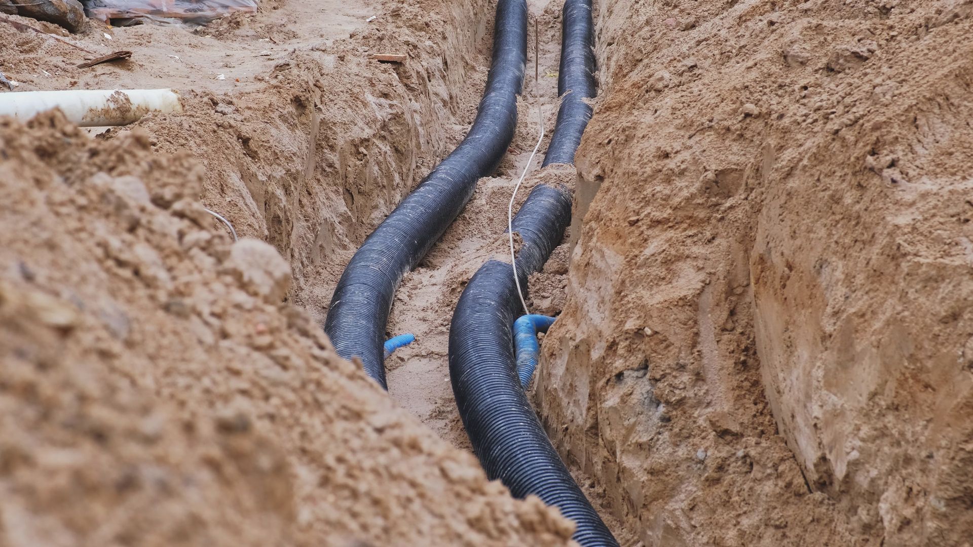 Des tuyaux noirs ondulés dans une tranchée sablonneuse.