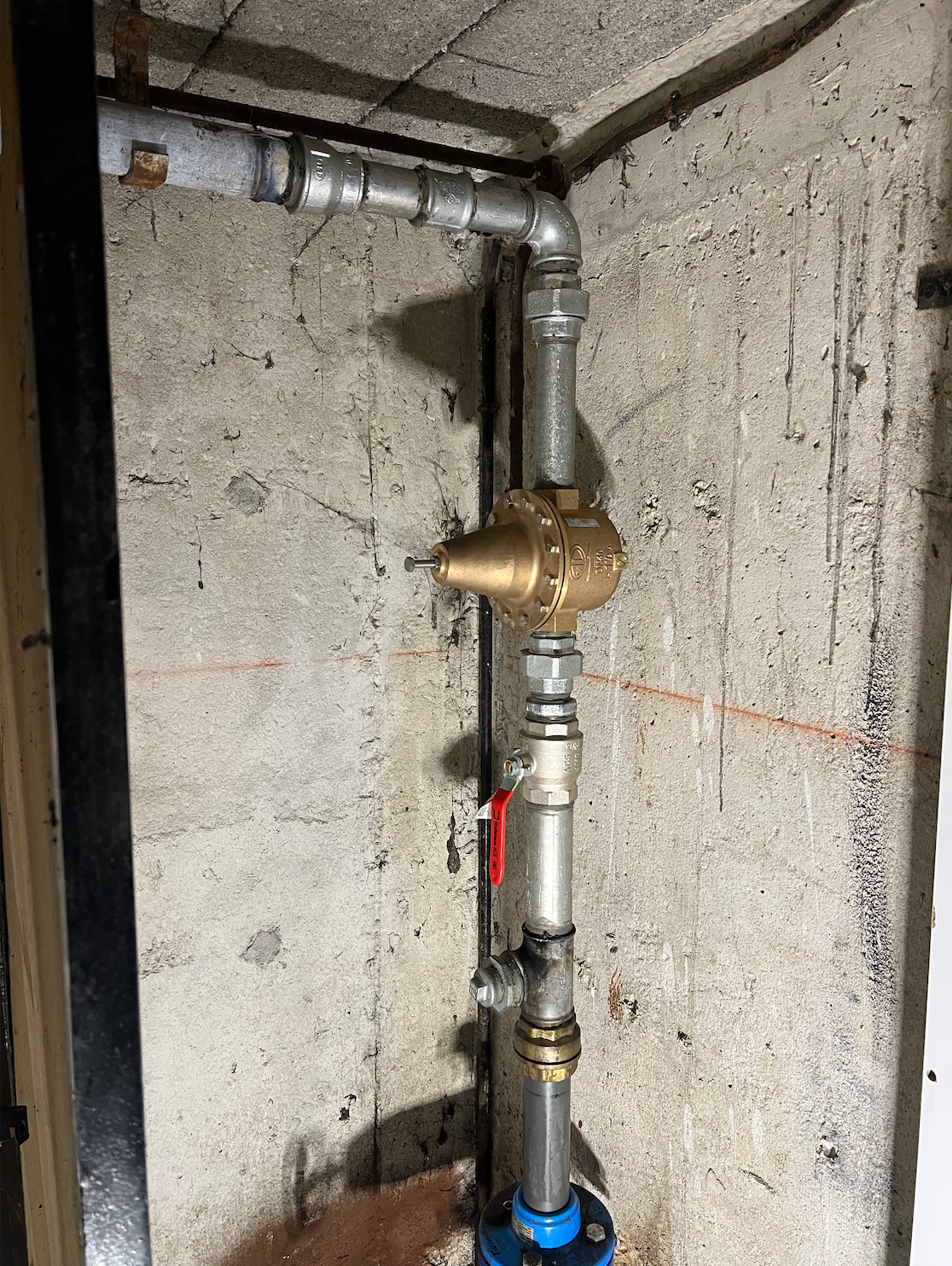 Système de plomberie avec régulateur de pression en laiton, tuyaux et vanne d'arrêt contre un mur en béton.