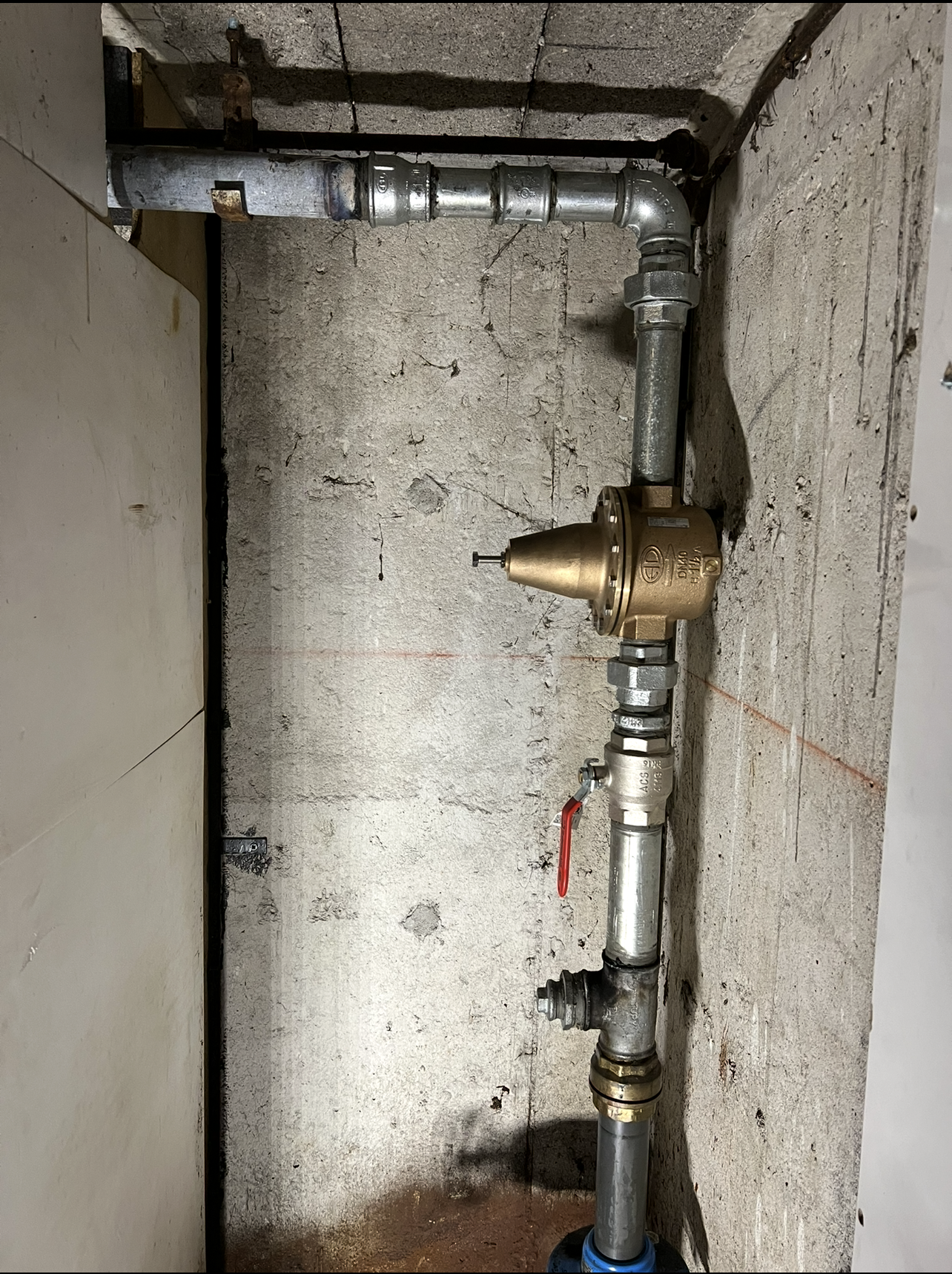 Tuyaux et régulateur de pression dans un mur en béton. Tuyaux métalliques et raccords en laiton visibles.