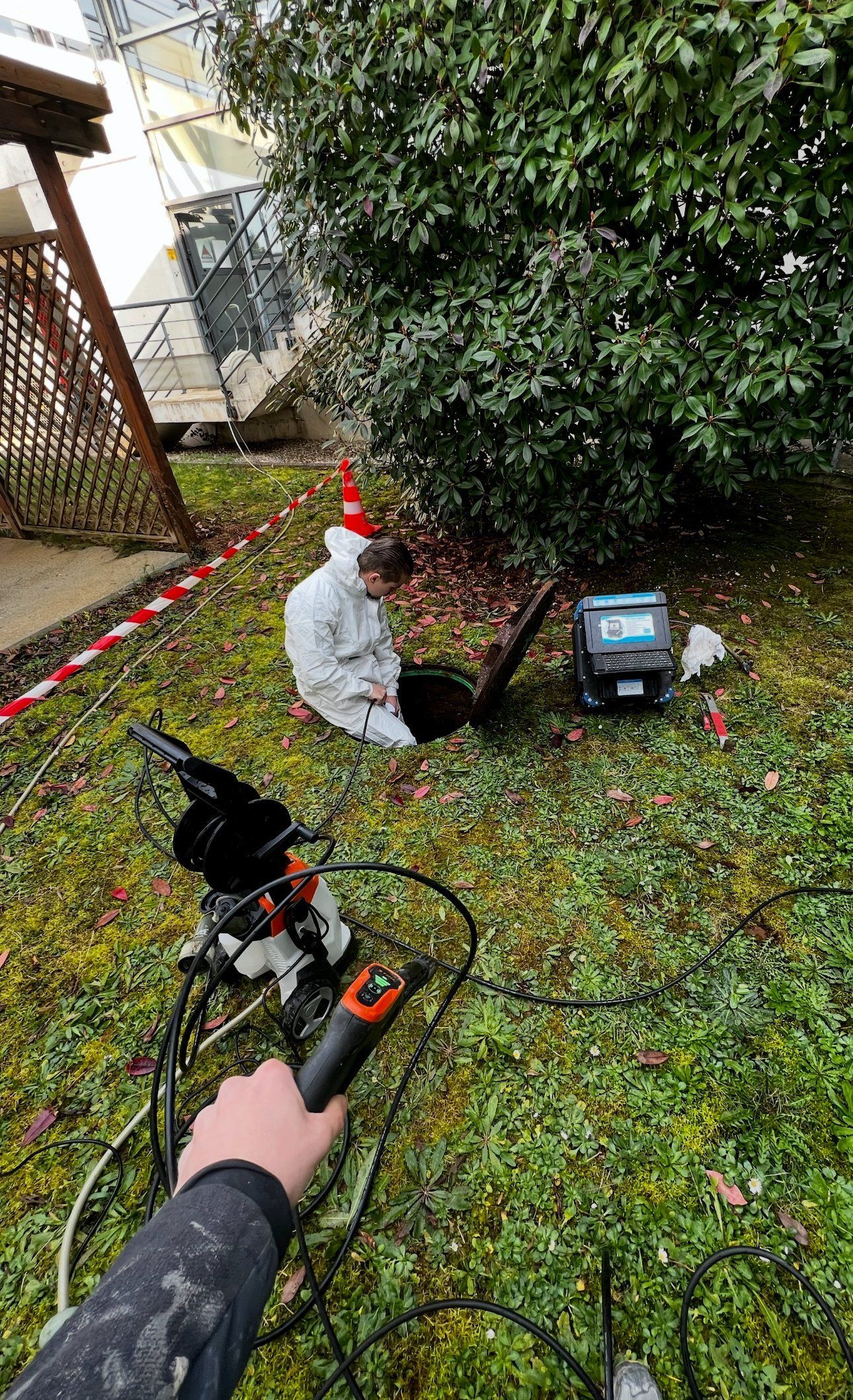 Une personne en tenue de protection, près d'un trou dans le sol, utilise un appareil à écran.