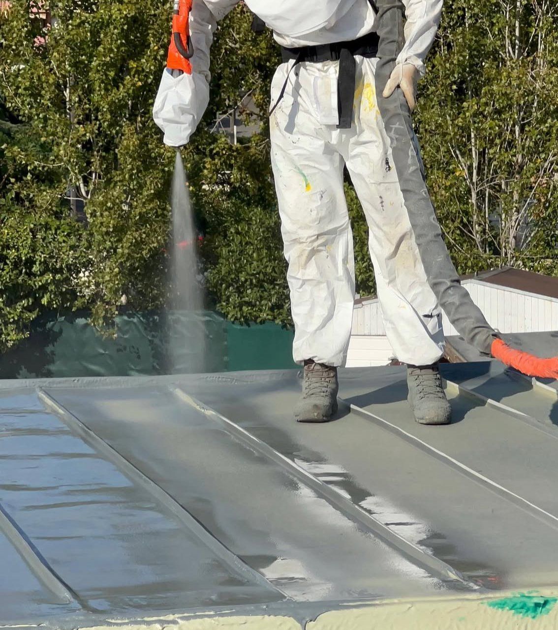 Personne en combinaison de protection pulvérisant un toit.