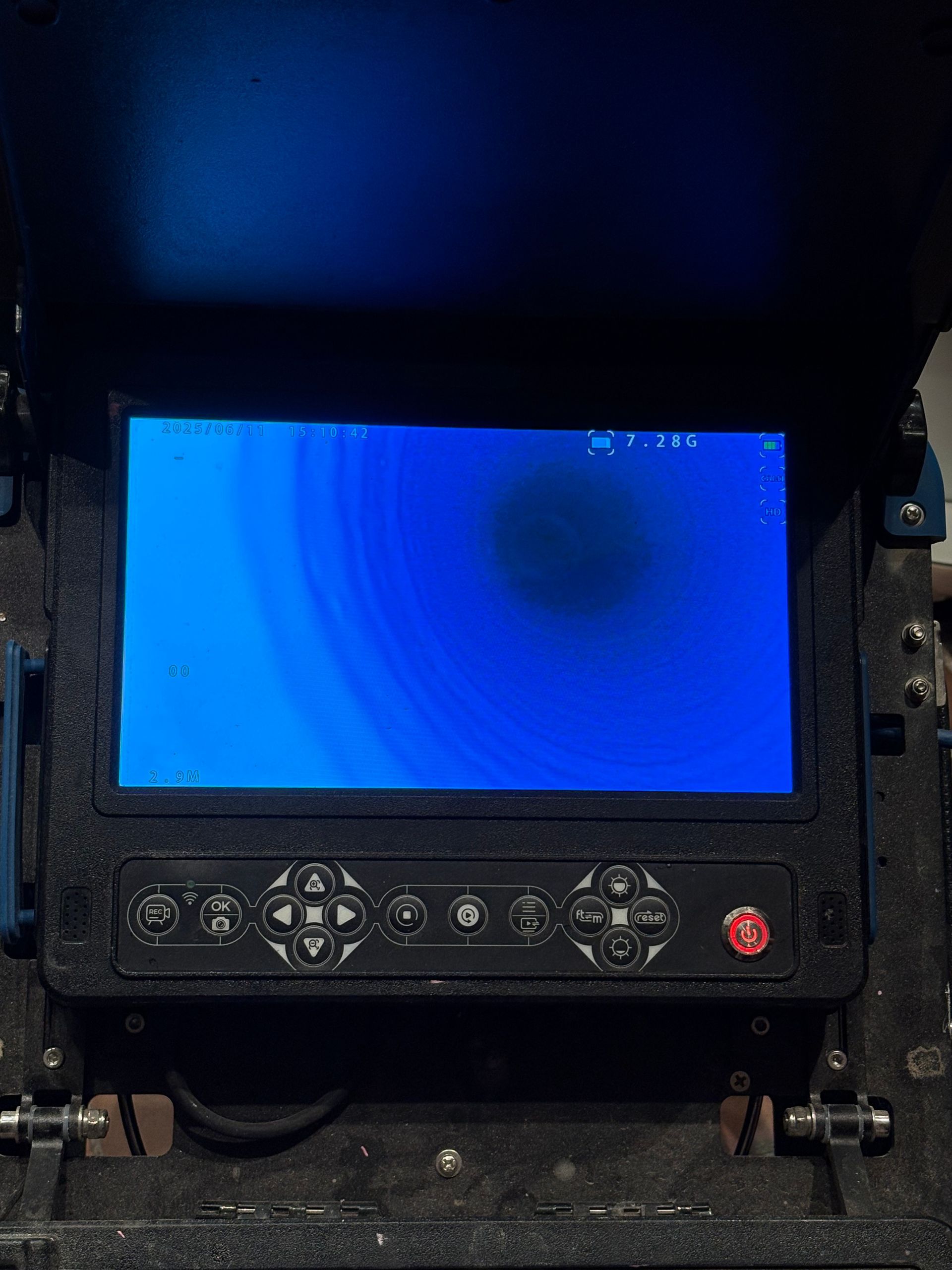 Panneau de commande noir avec écran bleu, boutons et bouton d'arrêt d'urgence rouge.