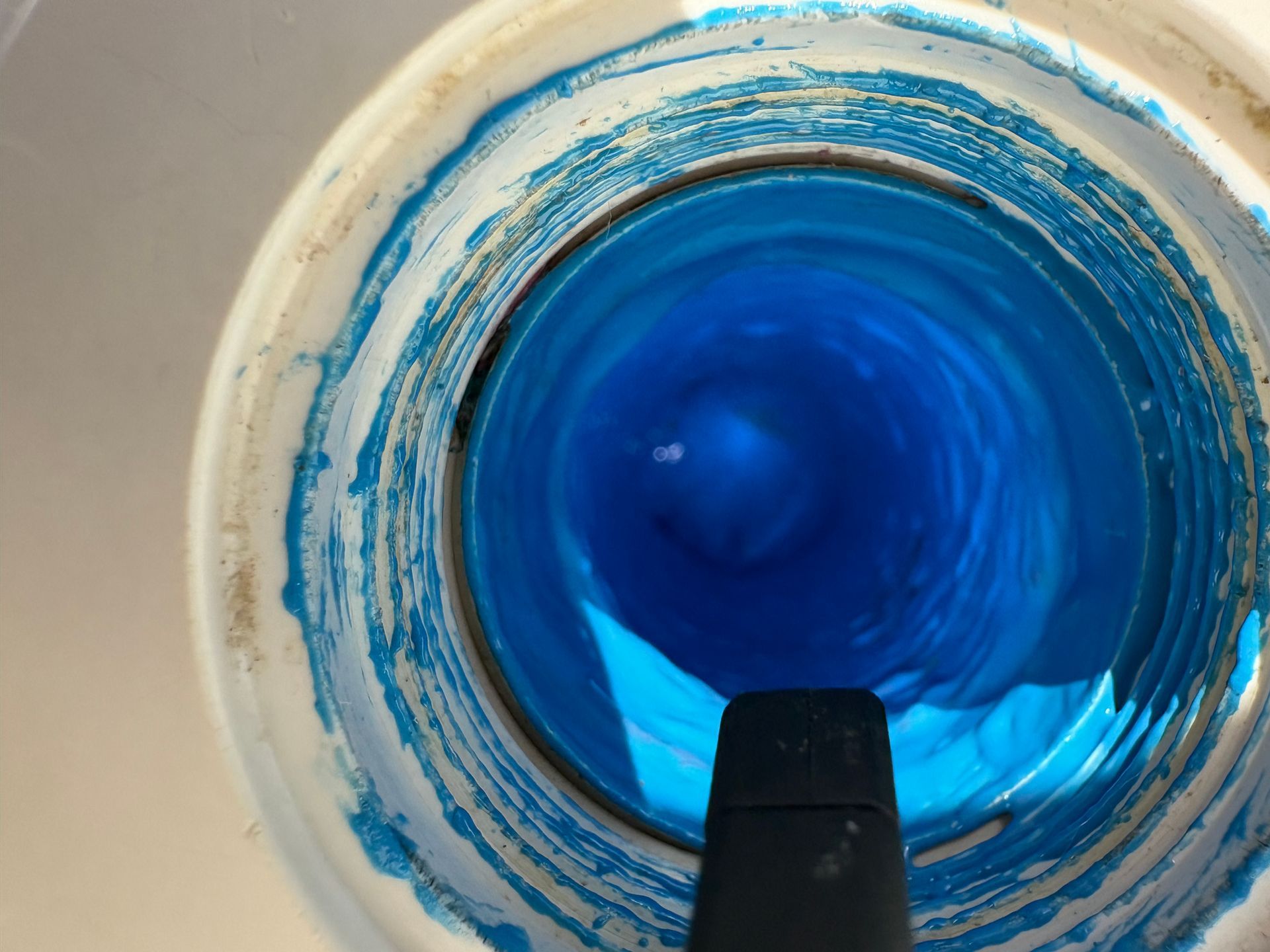 Vue plongeante sur un récipient rond rempli de liquide bleu. Le bord du récipient est blanc strié de bleu.