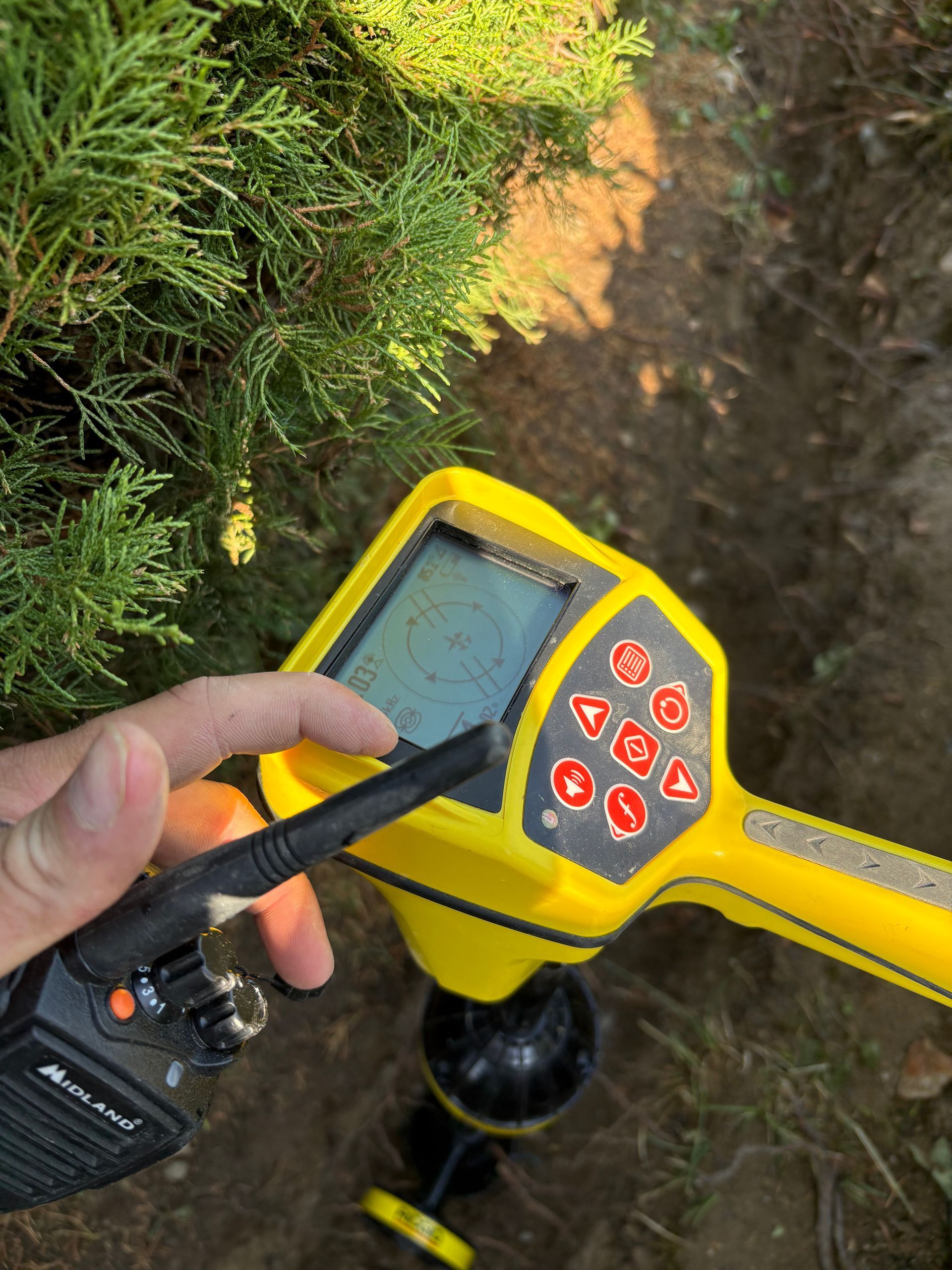 Main tenant un talkie-walkie près d'un détecteur de métaux jaune.