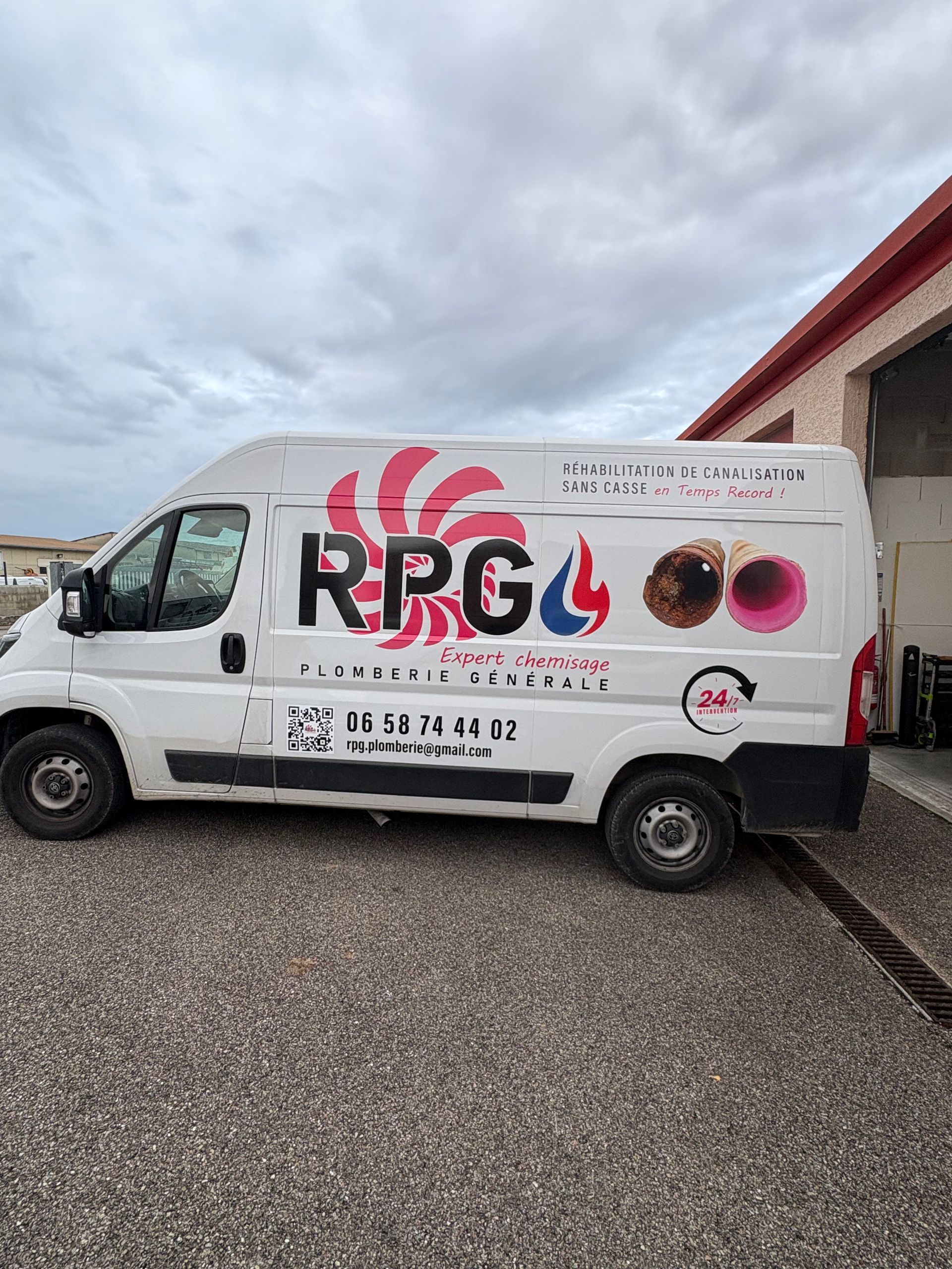 Une camionnette blanche avec le logo  RPG  et un numéro de téléphone, garée près d'un bâtiment.