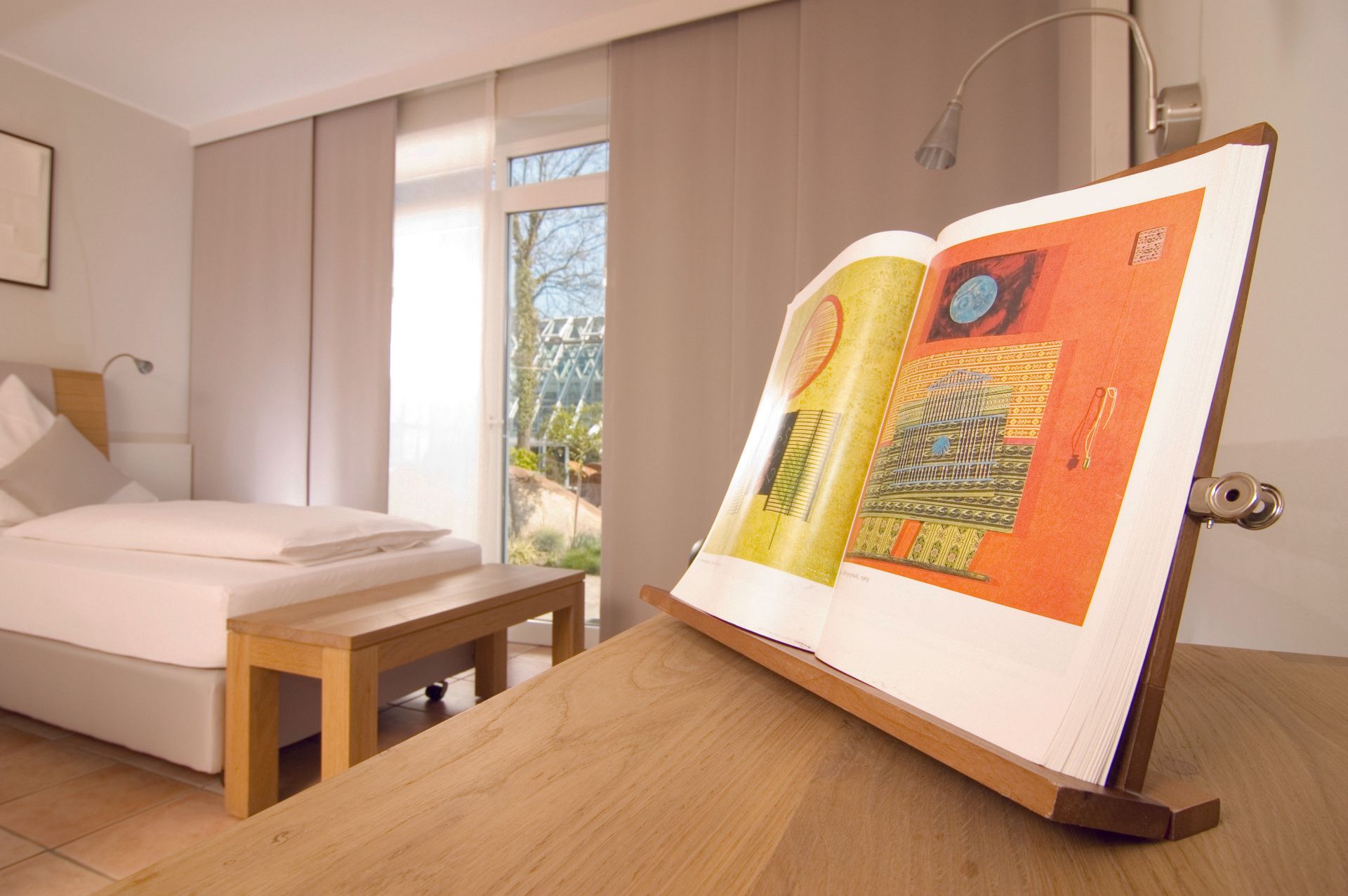 In einem Schlafzimmer liegt auf einem Holztisch neben einem Bett ein Buch.