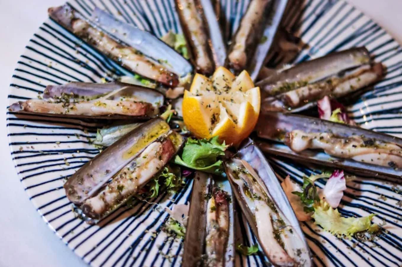Plato de navajas cocidas, adornadas con hierbas y una rodaja de limón.