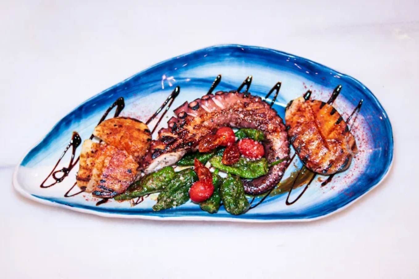 Pulpo a la parrilla y guarniciones en plato azul ovalado con glaseado balsámico.
