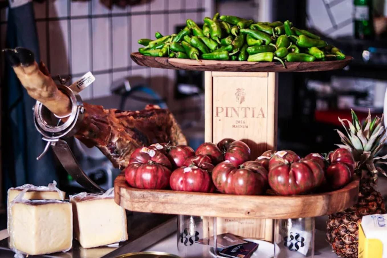 Exhibición gastronómica con tomates, pimientos, jamón ibérico, queso y piña.