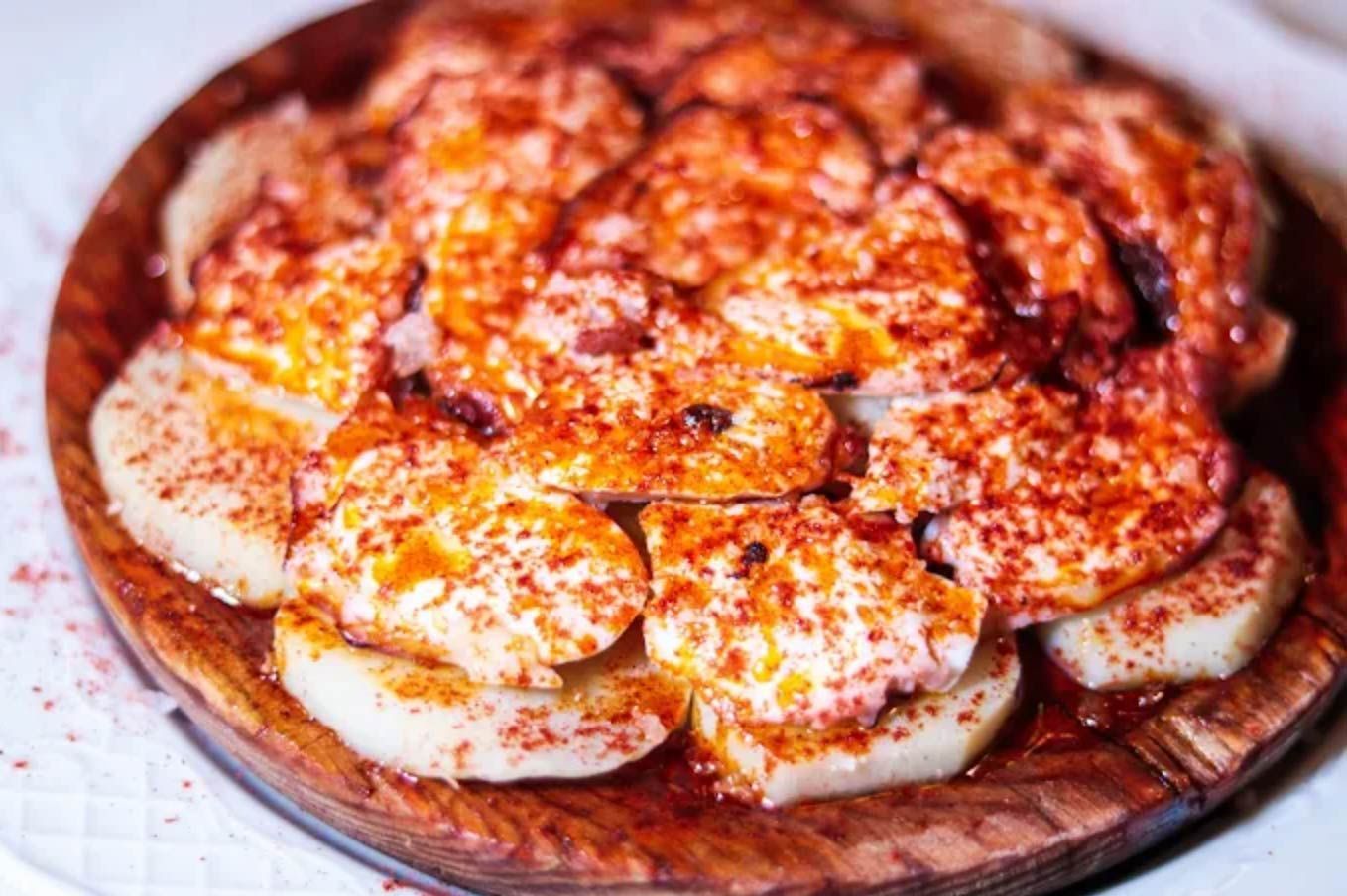 Patatas cortadas en rodajas con pimentón, servidas en un plato de madera.