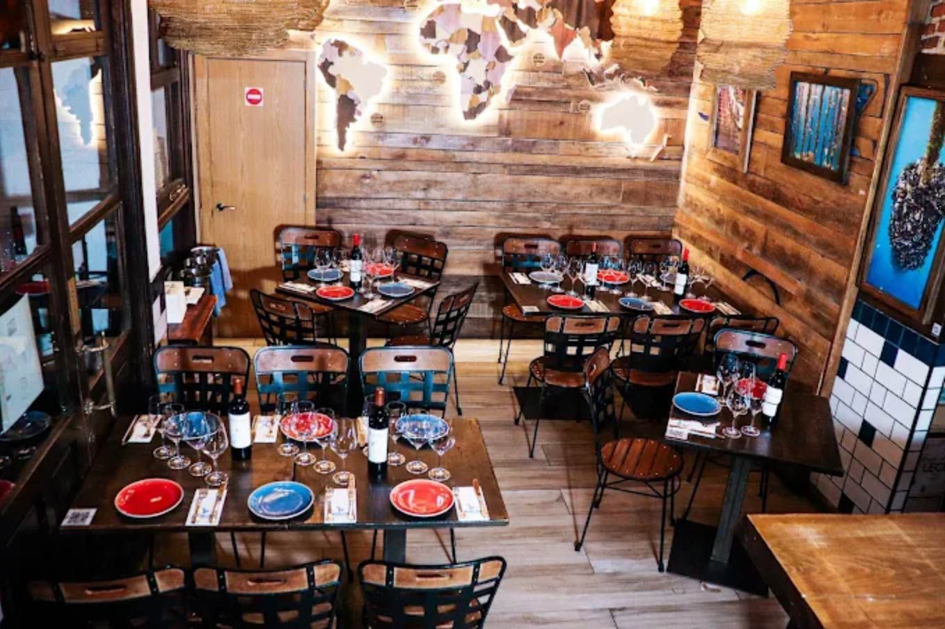 Interior de restaurante con mesas preparadas para los comensales; decoración de mapa del mundo en pared de madera rústica.