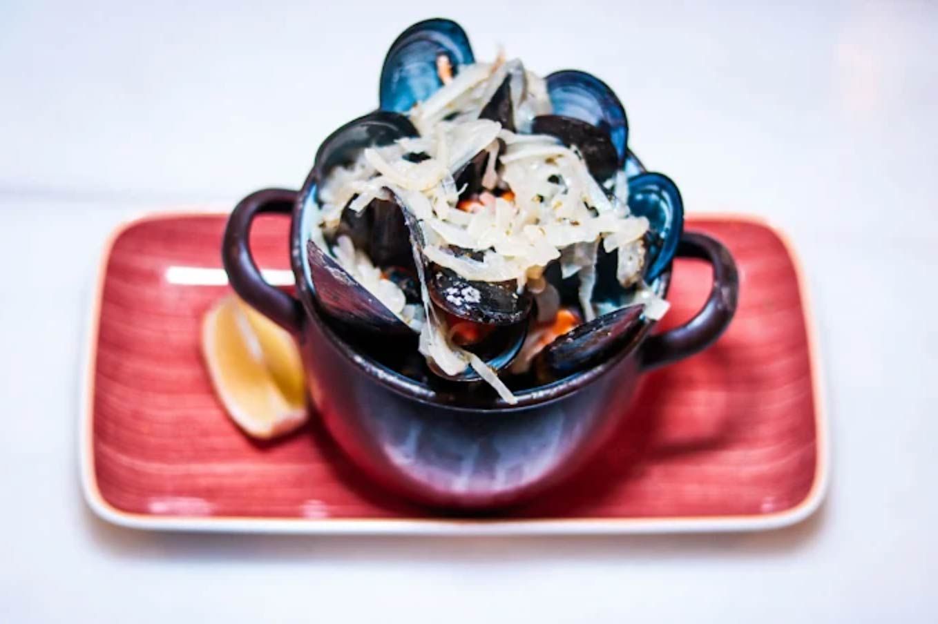Plato de mejillones con queso, servido con rodaja de limón en un plato rojo.